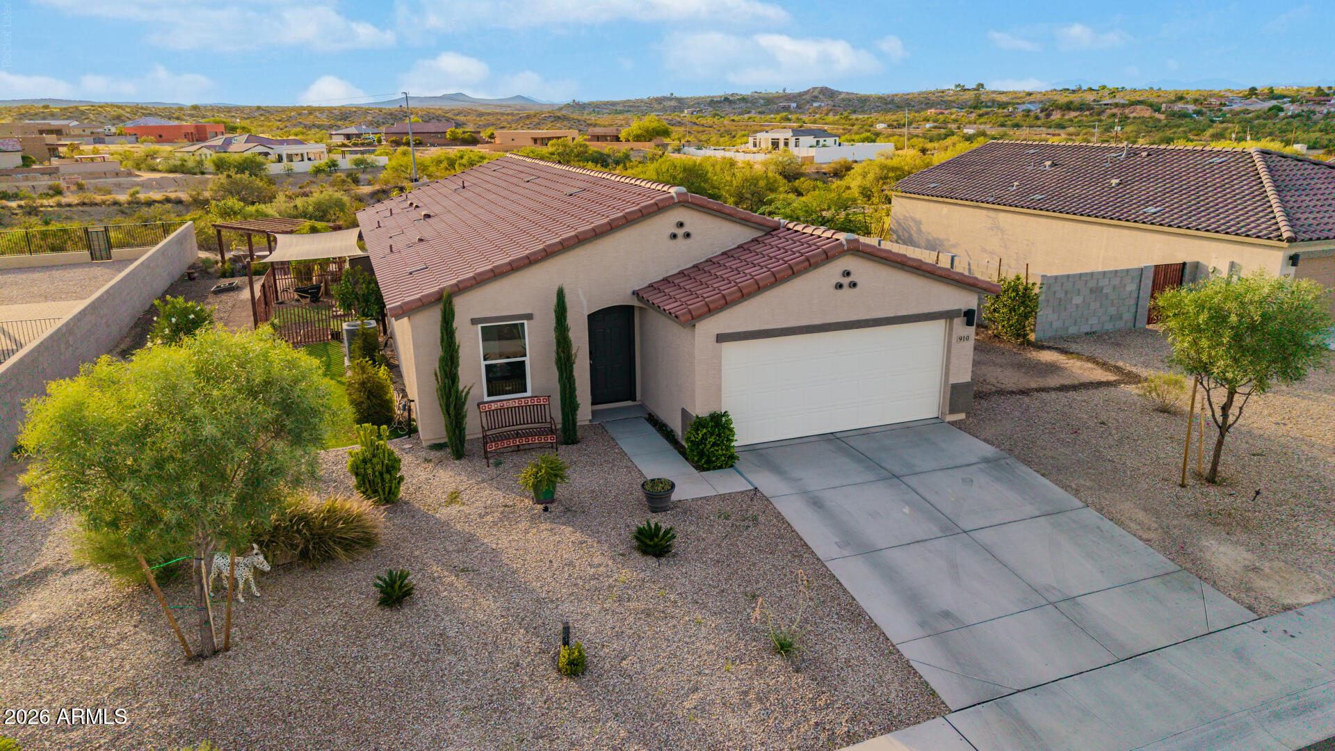 Single-story stucco home with a red tile roof, two-car garage, gravel landscaping, and desert hills beyond.