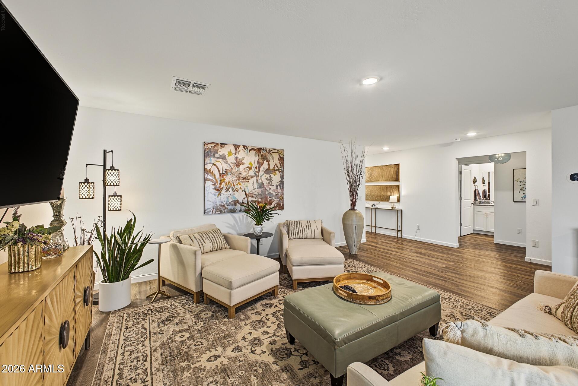 Furnished living room with cream chaise lounges, patterned rug, wood floors, and an adjoining doorway.