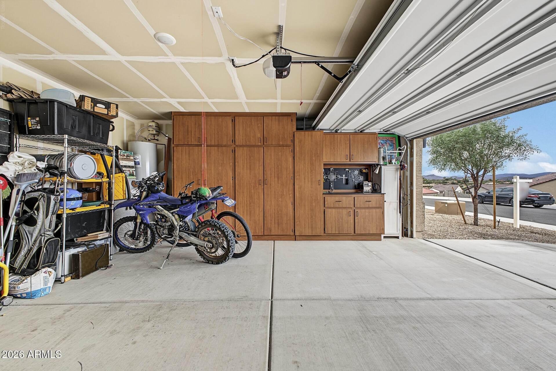 Garage with extensive wooden cabinets, motorcycles, and storage shelving beside an open overhead door.