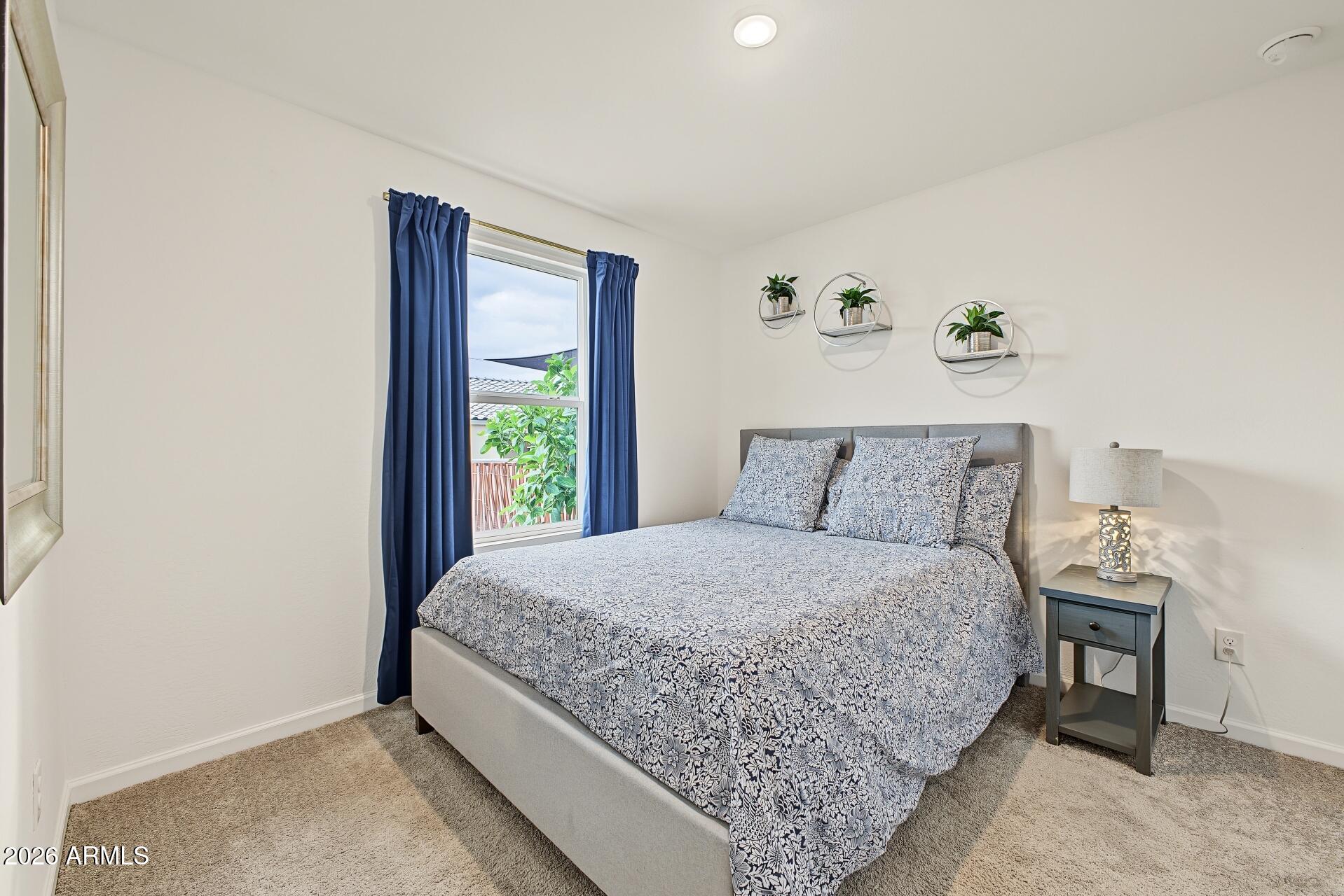 Furnished bedroom with patterned bedding, navy curtains, and circular wall shelves holding plants.