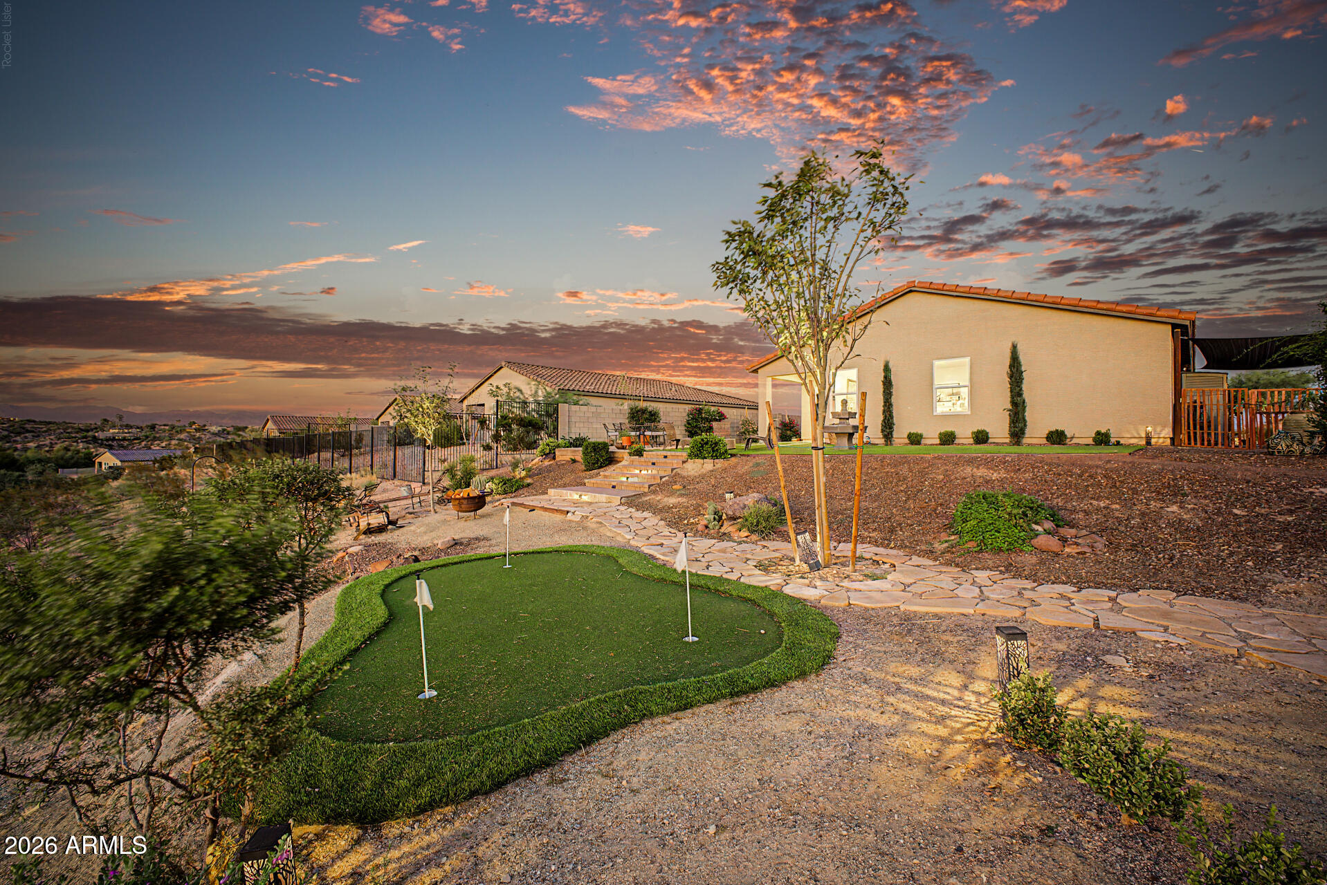 Single-story home at dusk with a stone path, patio seating, and a small putting green.