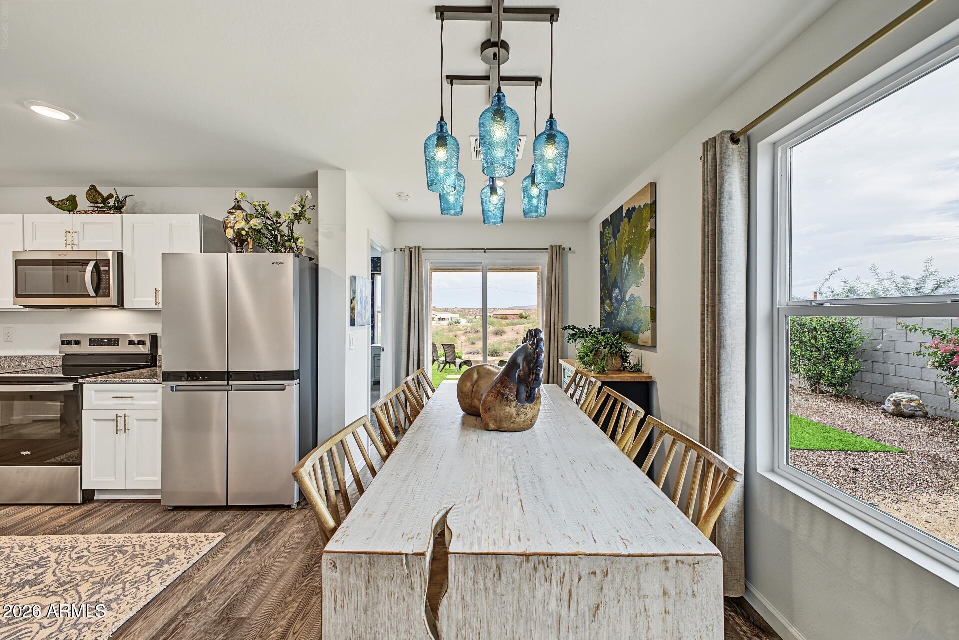 Dining area with a long rustic table, blue pendant lights, and an adjoining white kitchen.