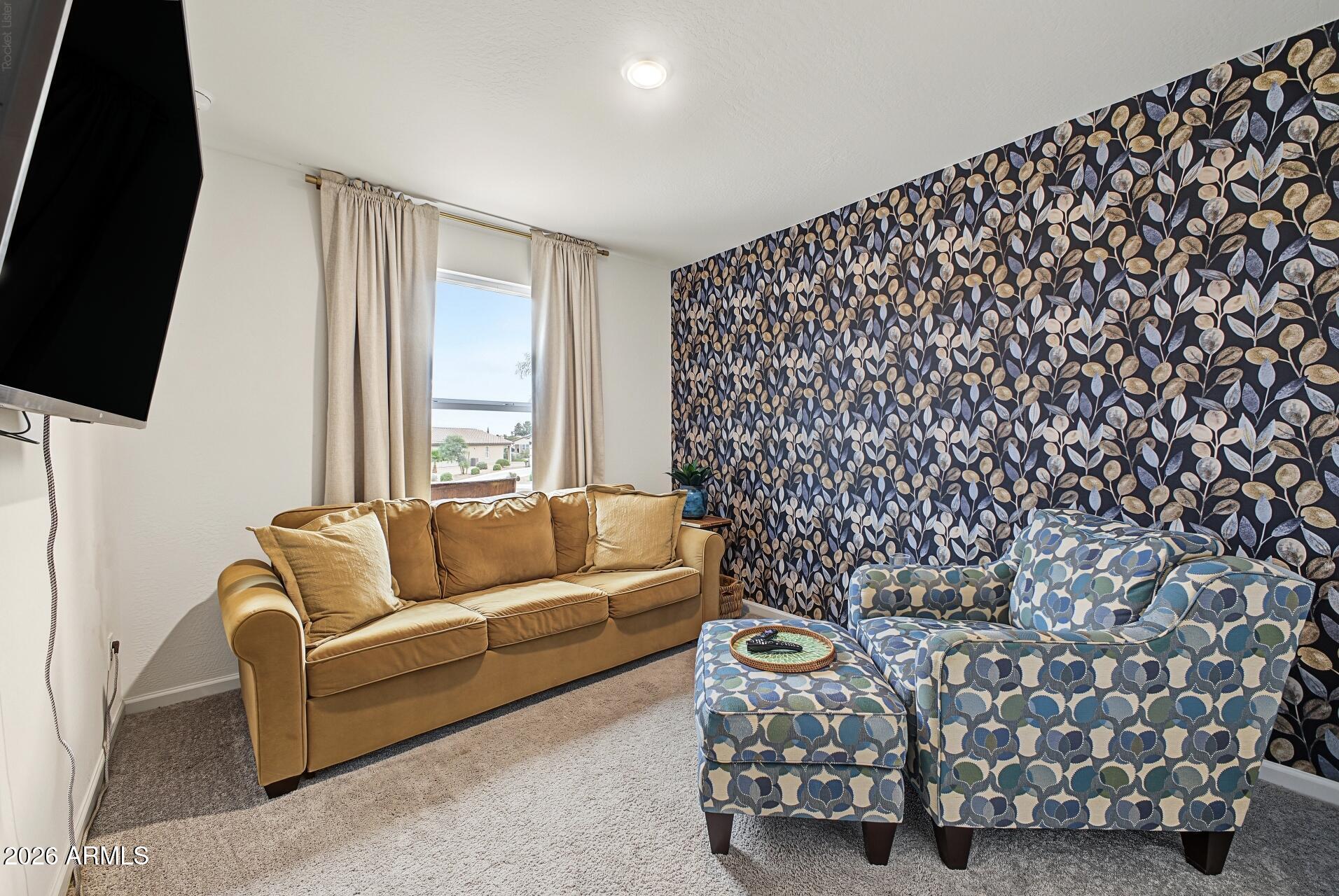 Living room with a tan sofa, patterned seating, and a dark botanical accent wall.