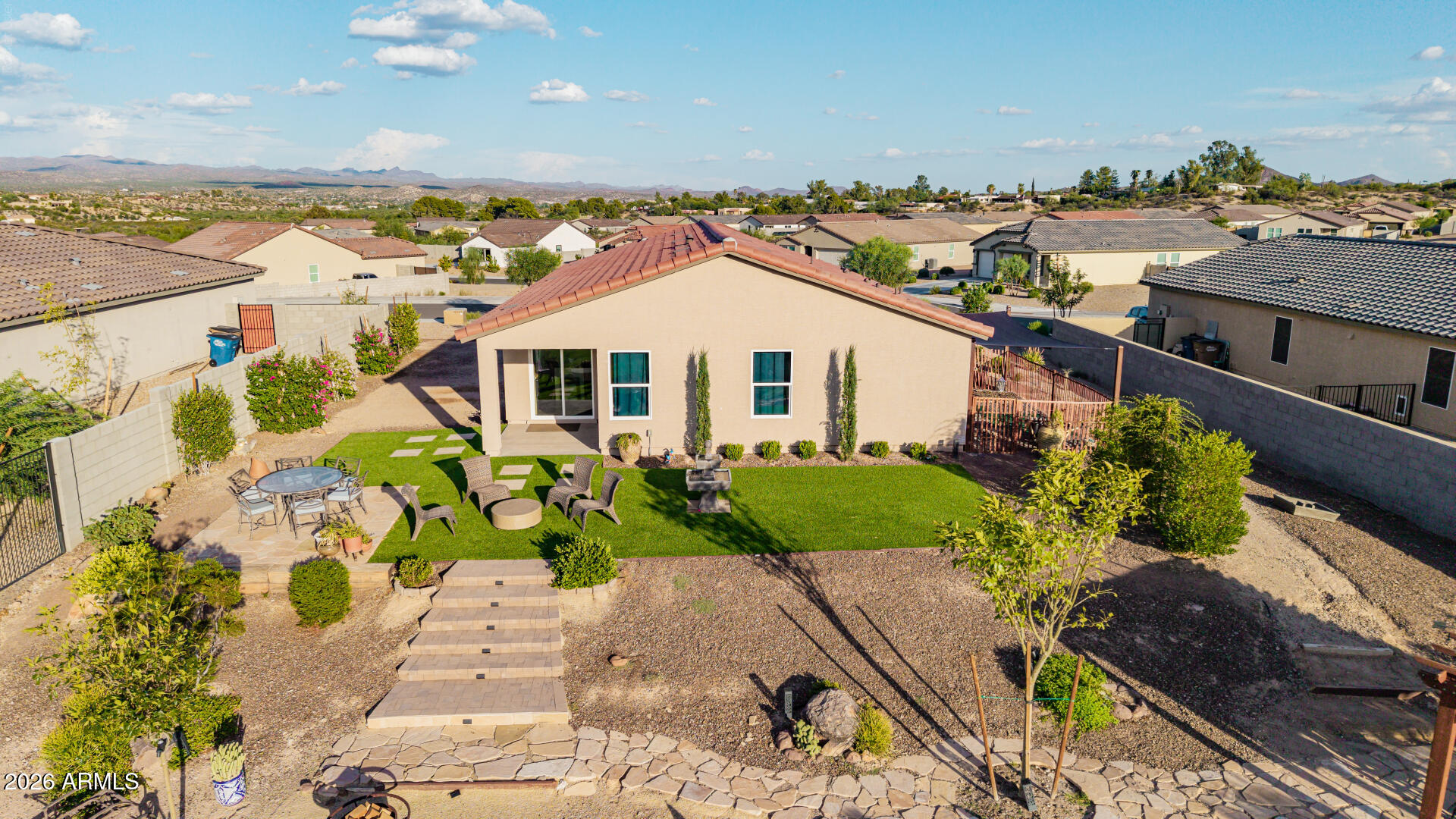 Rear of a single-story home with a turf lawn, patio seating, and distant mountain views.