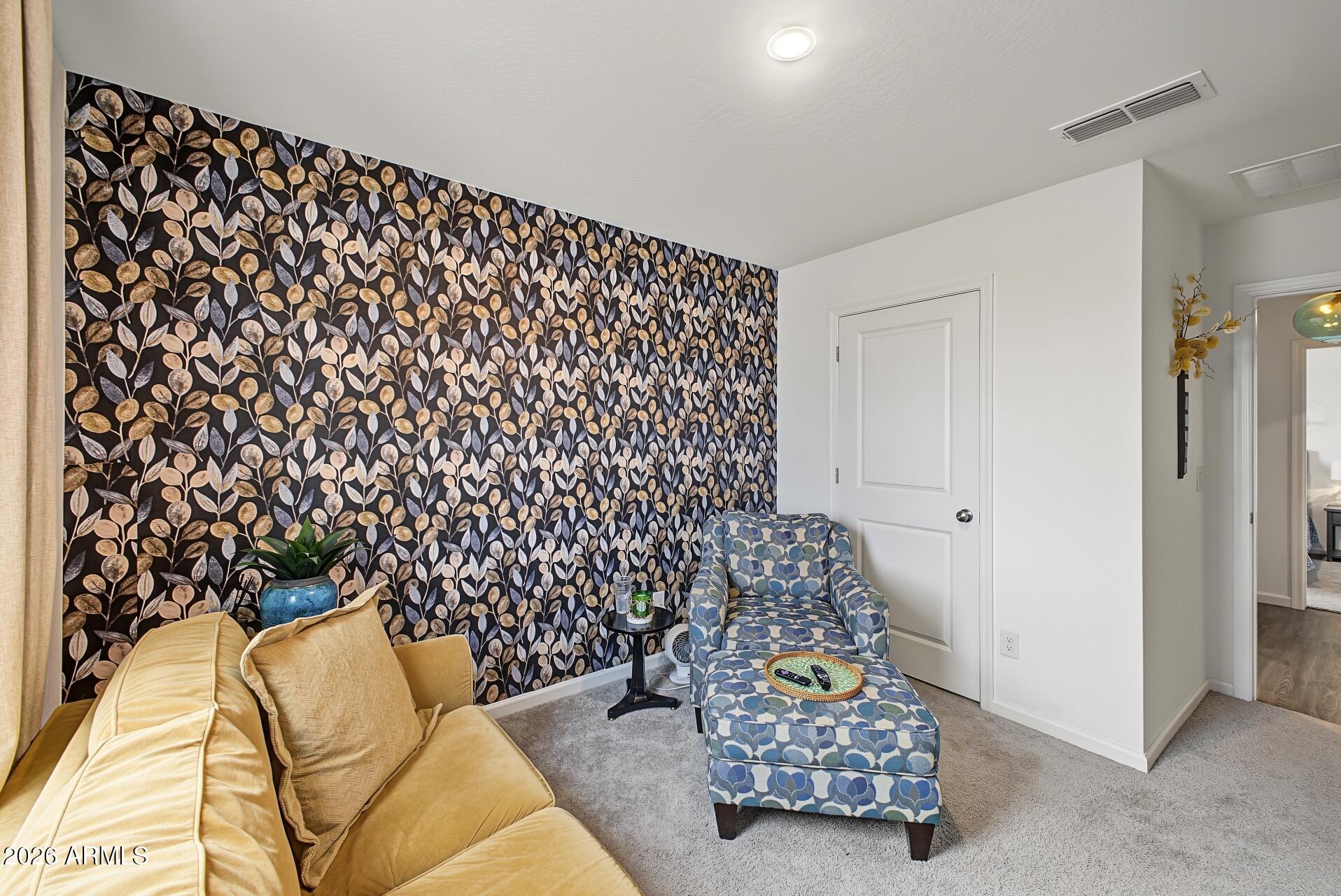 Sitting room with botanical wallpaper, a mustard sofa, and a blue patterned armchair and ottoman.