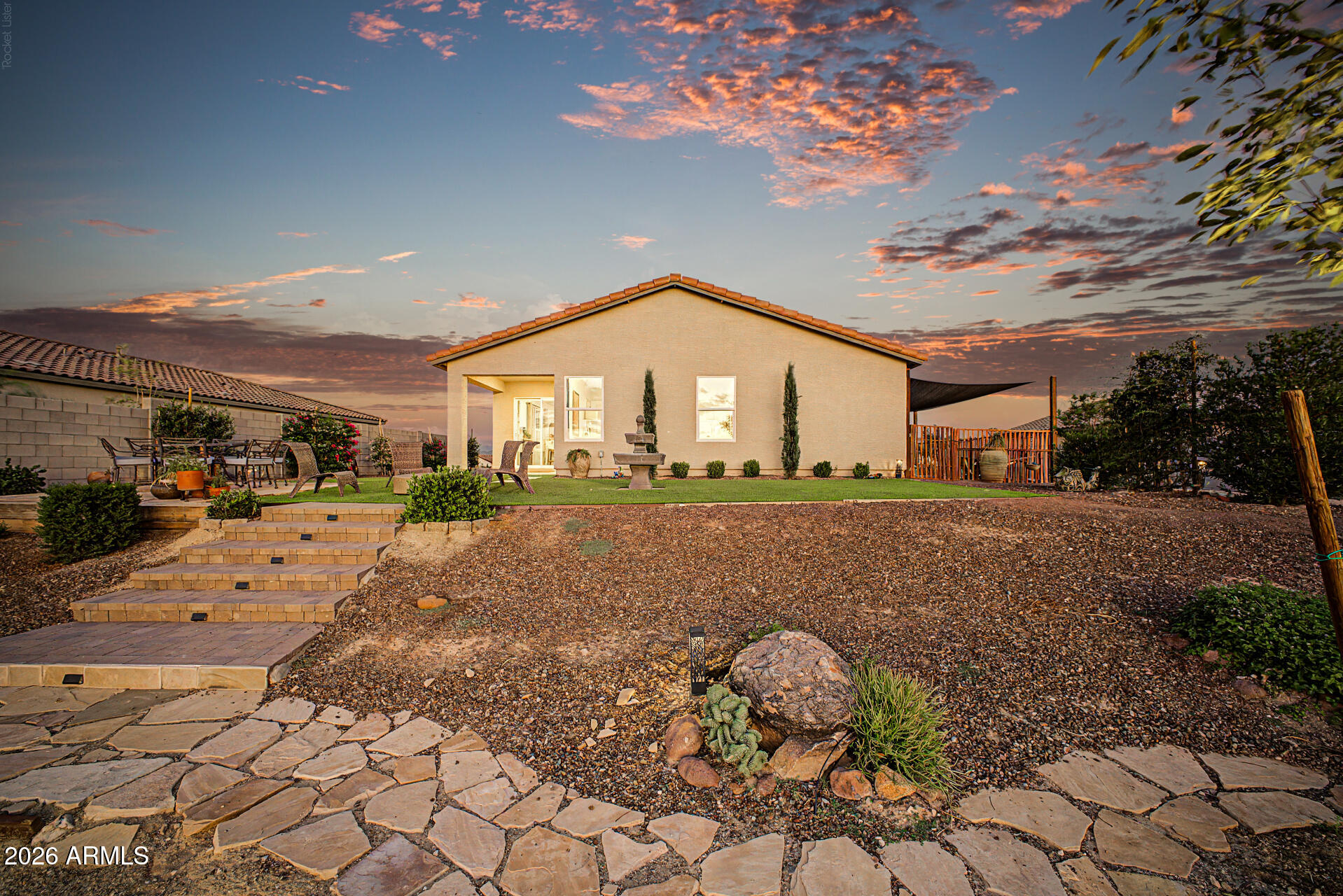 Home’s backyard at sunset, with stone steps, gravel landscaping, patio seating, and a small fountain.