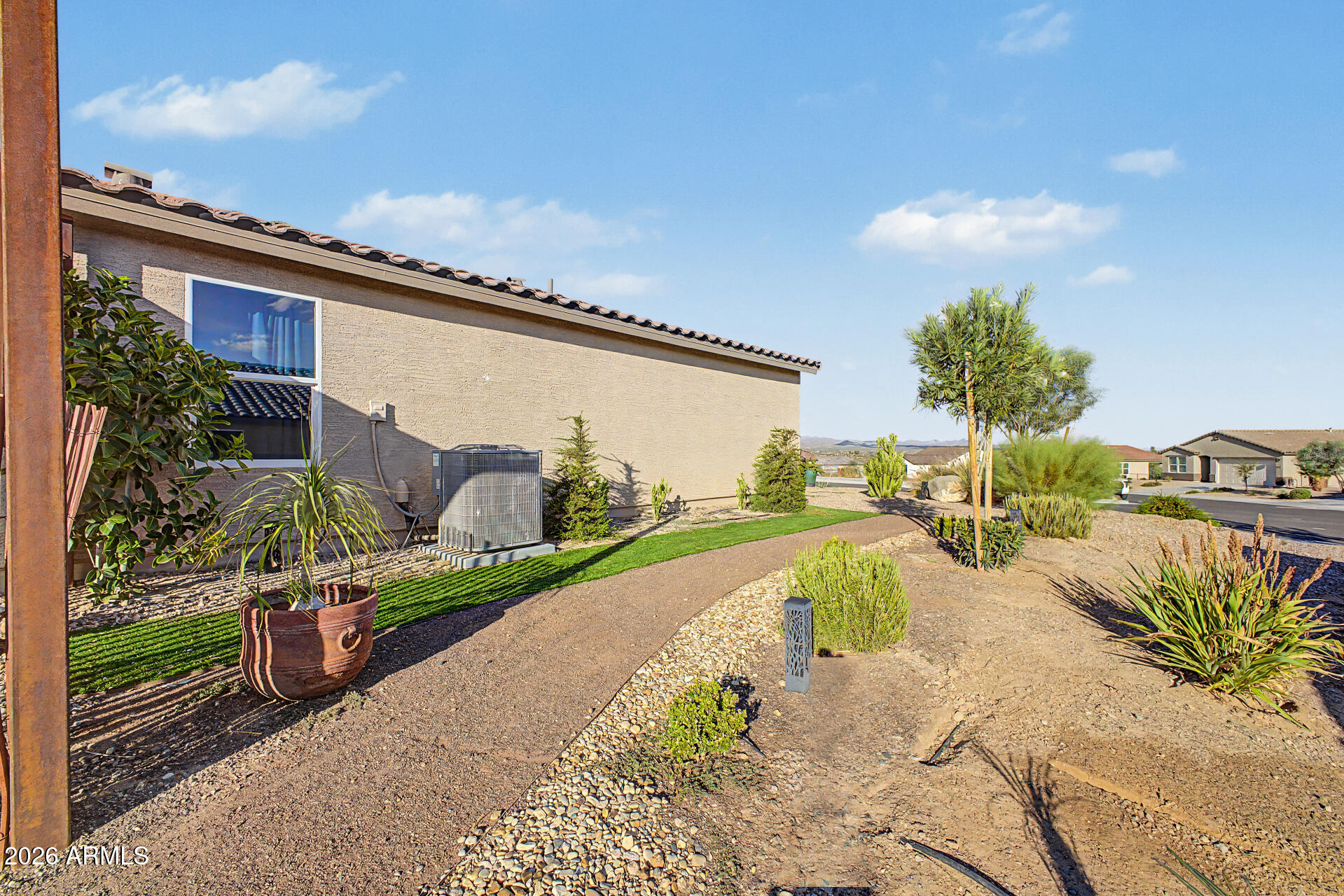 Home side yard with a gravel path, desert landscaping, and a strip of lawn.