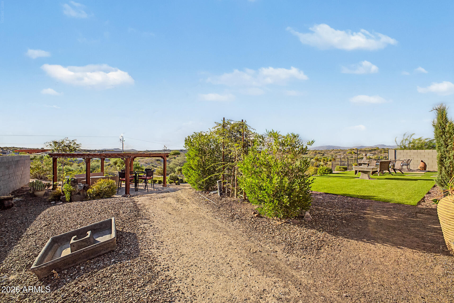 Backyard with a wooden pergola, green turf seating area, and distant desert hills.