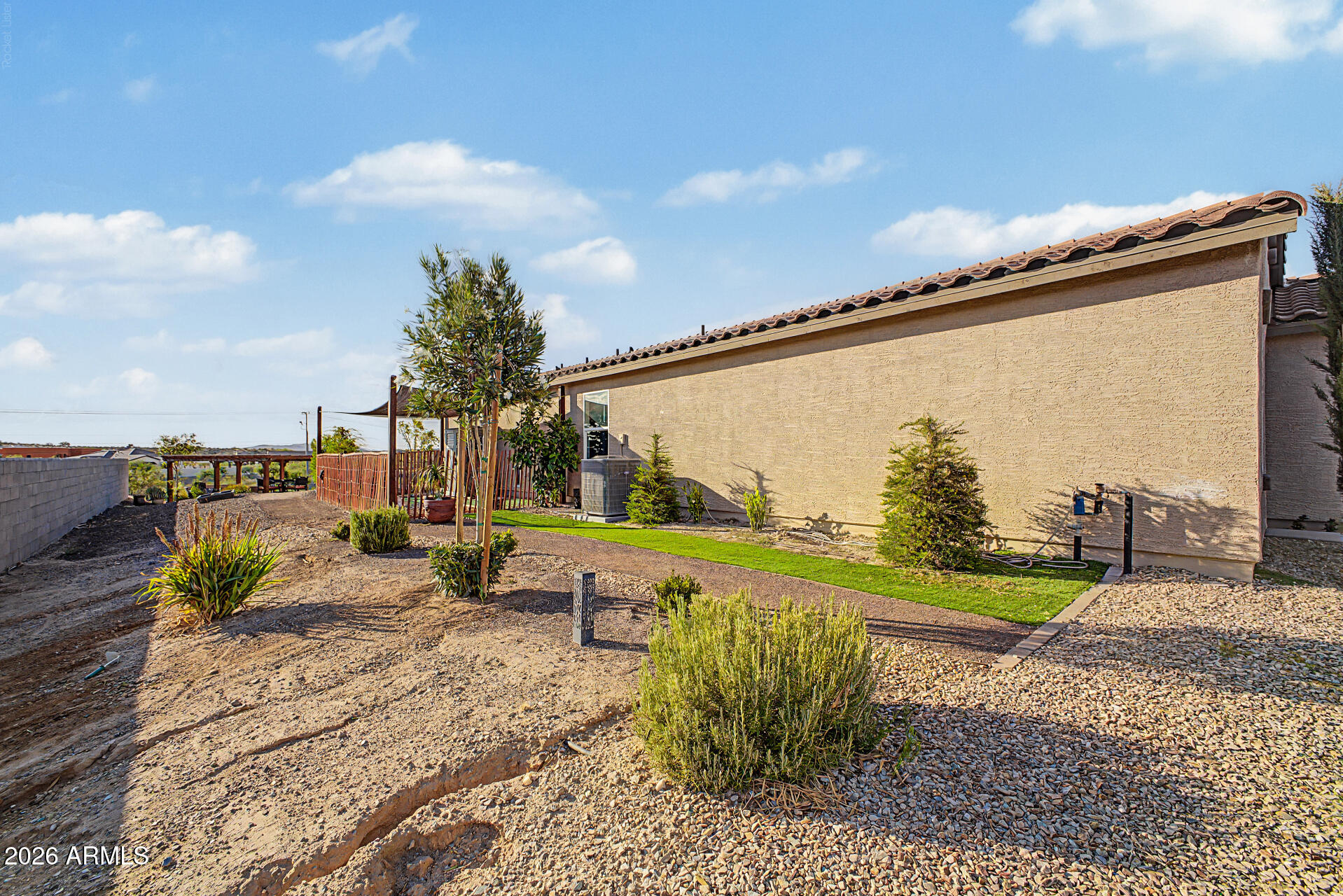 Stucco home exterior beside a gravel yard with shrubs and a narrow strip of lawn.