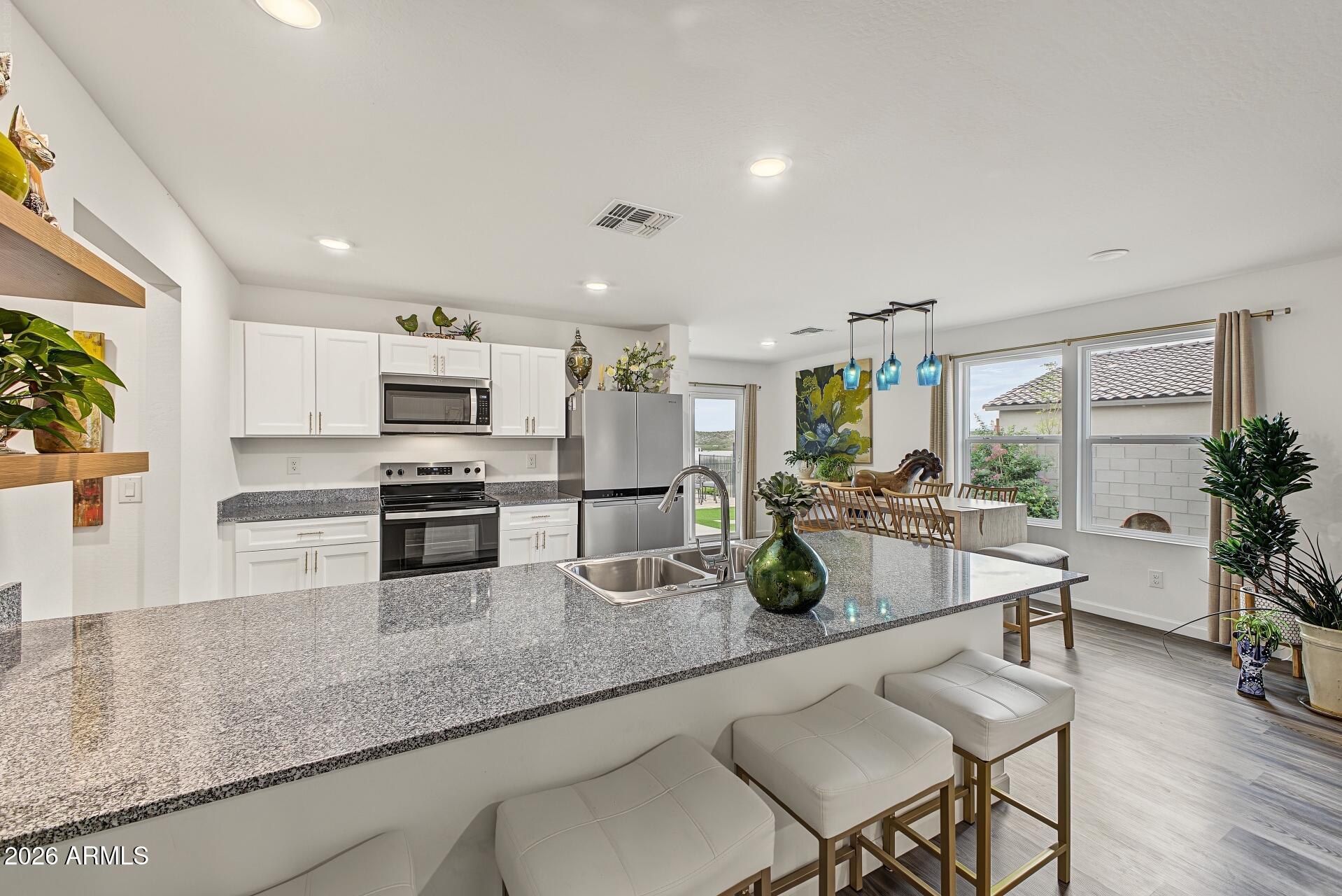 Open-plan kitchen with a granite island, white cabinets, stainless steel appliances, and adjoining dining area.