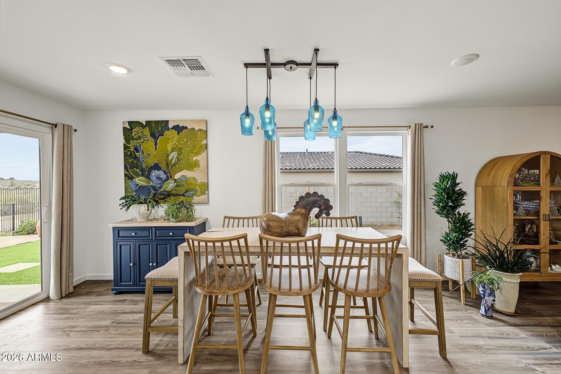 Dining room with a long wood table, blue pendant lights, navy sideboard, and large windows.