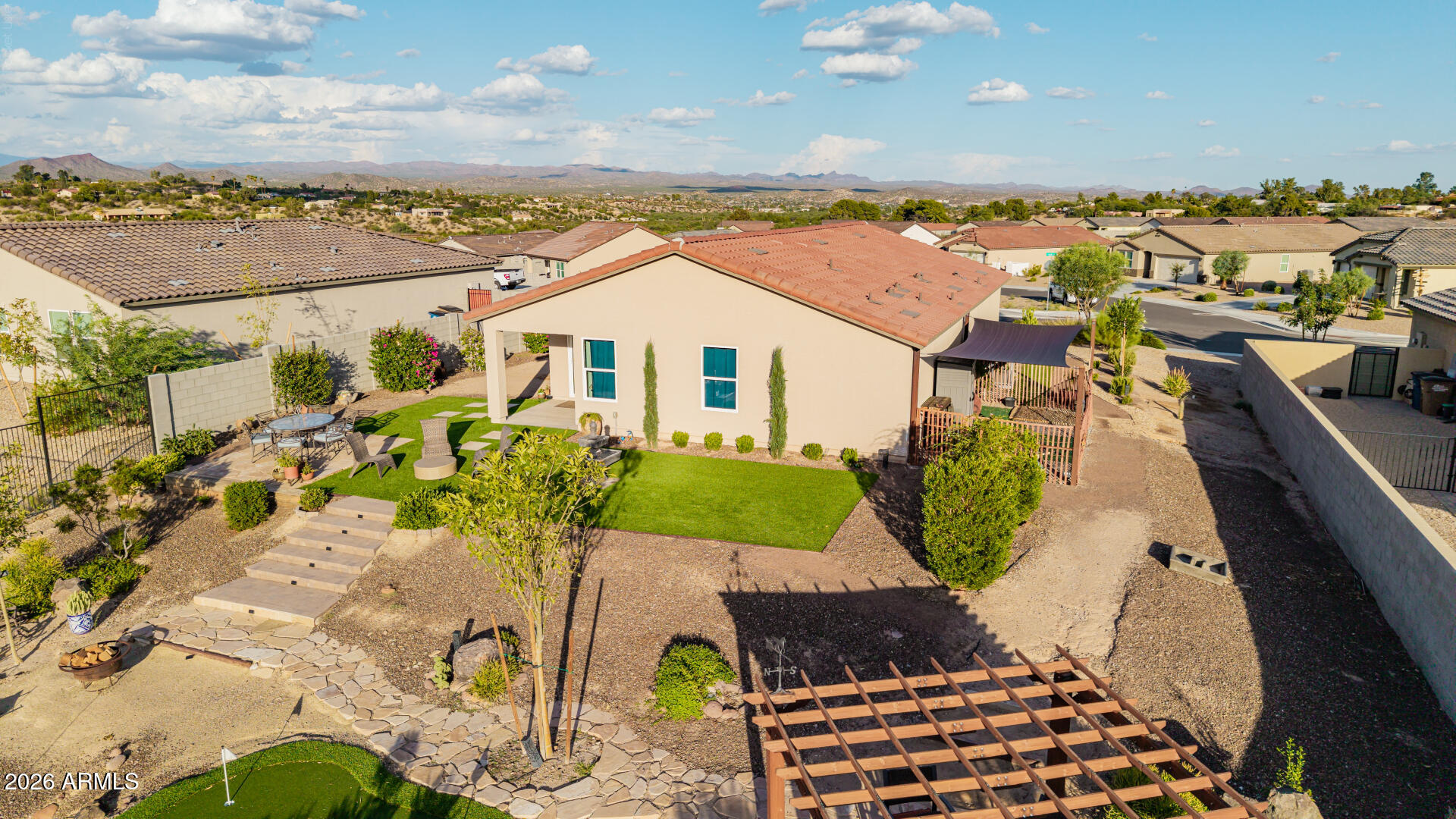 Aerial backyard view with a covered patio, artificial grass, desert landscaping, and distant mountains.