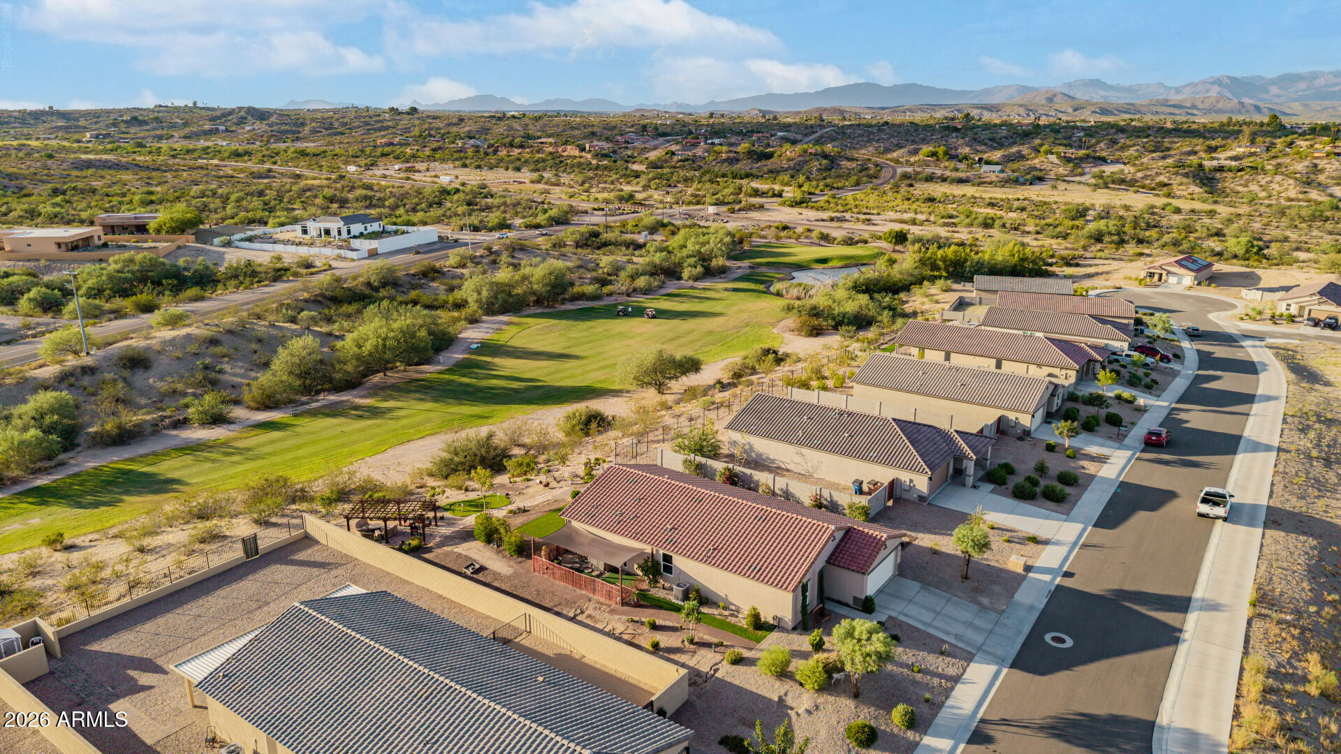 Aerial view of homes beside a green golf course, with desert hills and mountains beyond.