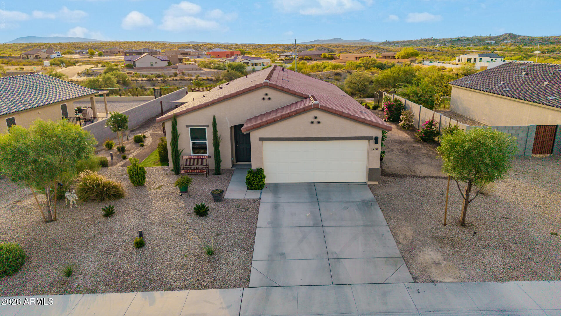 Aerial view of a stucco home with a two-car garage, gravel landscaping, and low hills beyond.