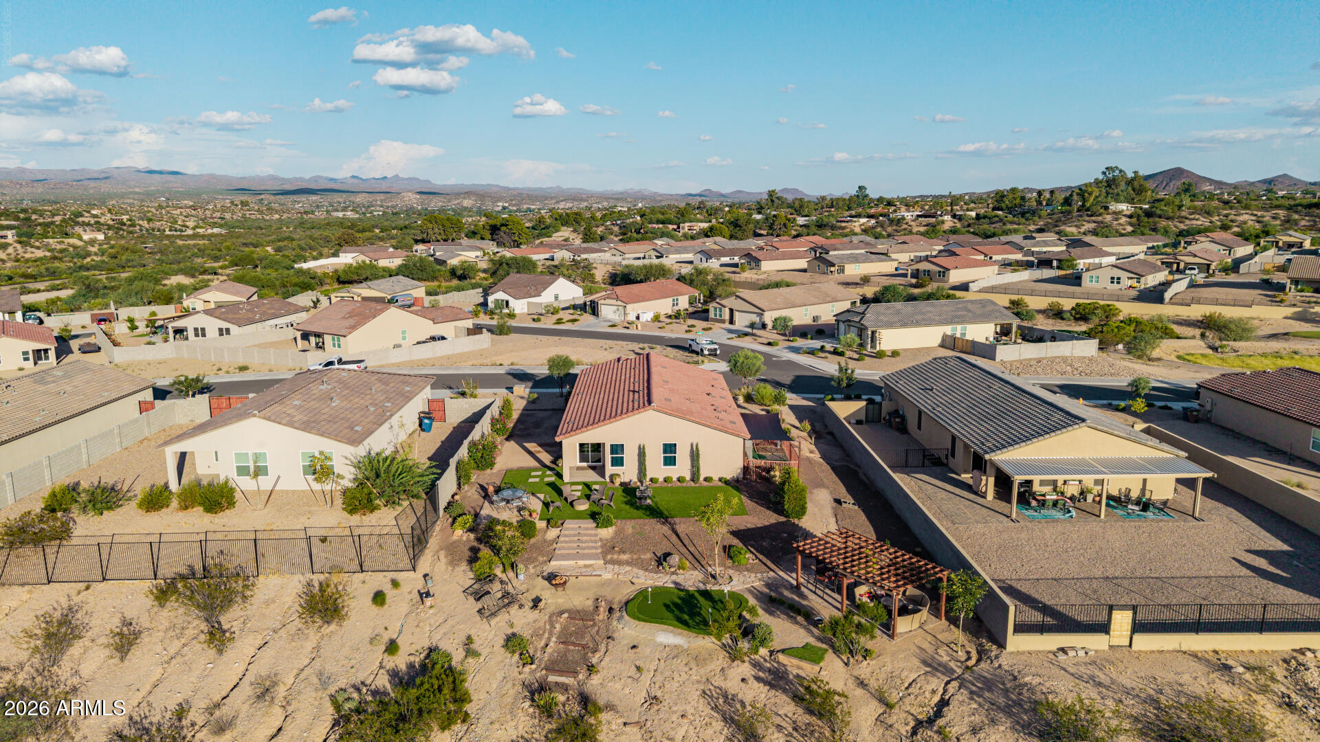 Aerial view of a Wickenburg home with a putting green, pergola, and desert mountains beyond.