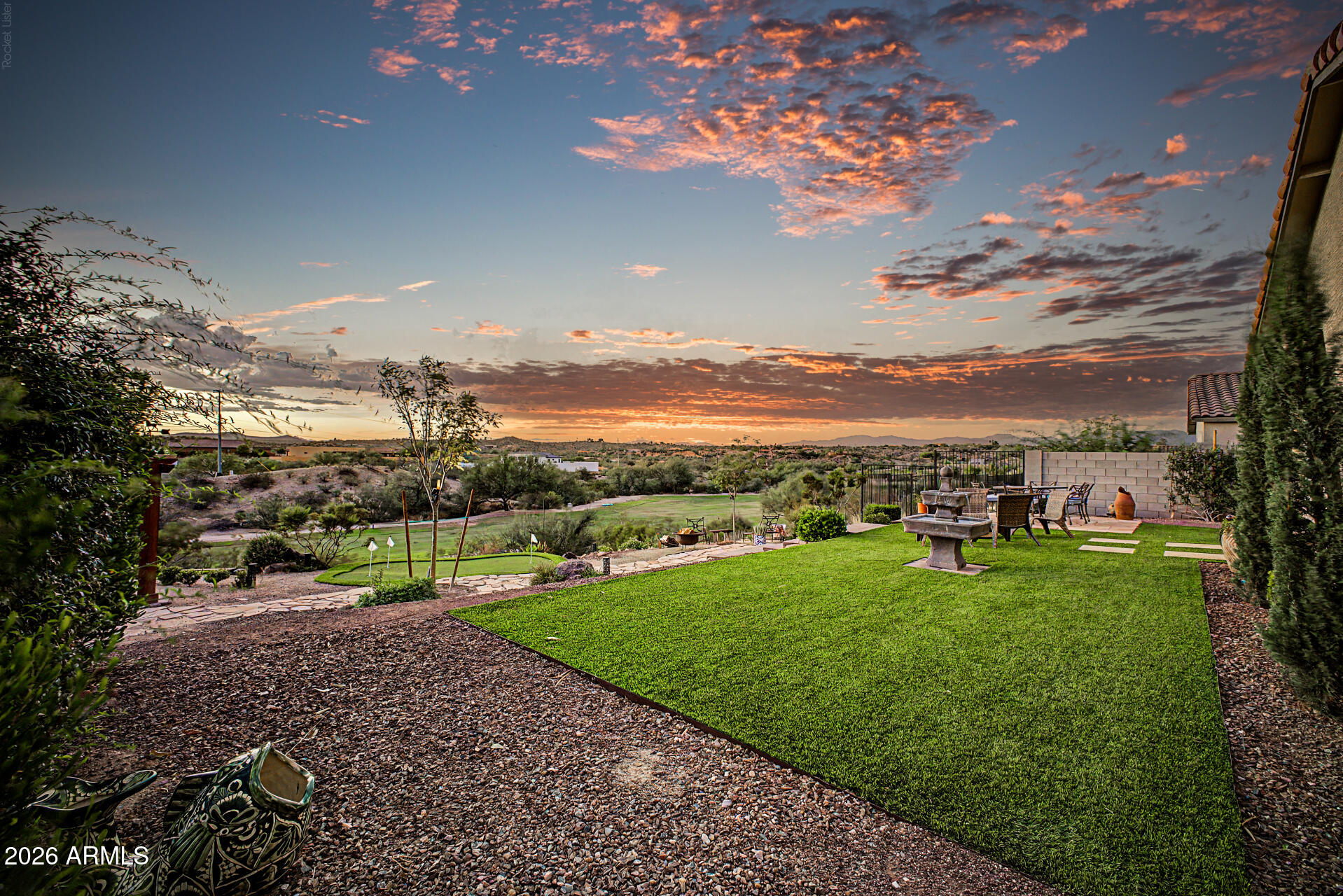 Backyard lawn and patio with a fountain, overlooking a golf course beneath a colorful sunset sky.