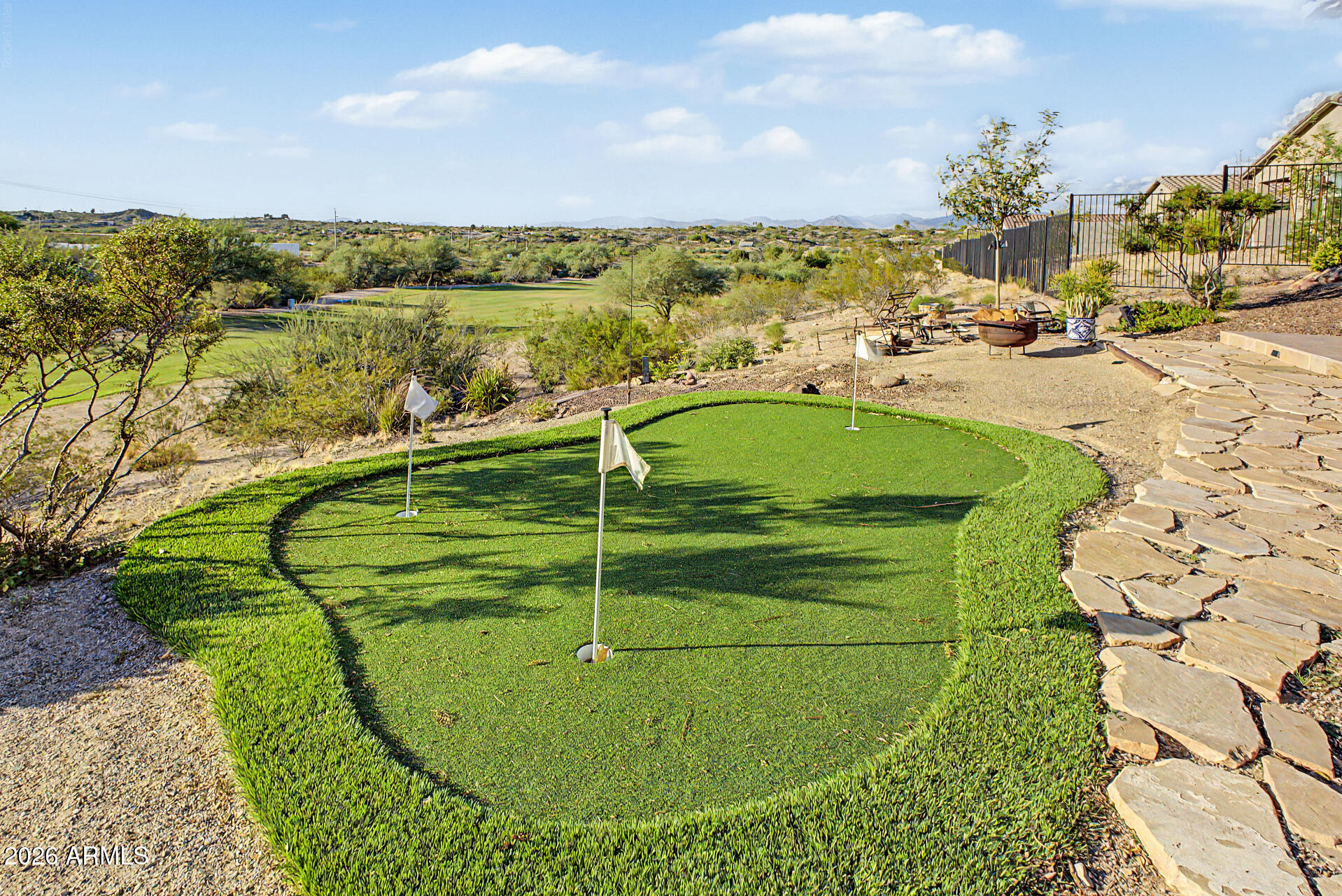 Backyard putting green with flagsticks and stone path, overlooking a golf course and desert hills.