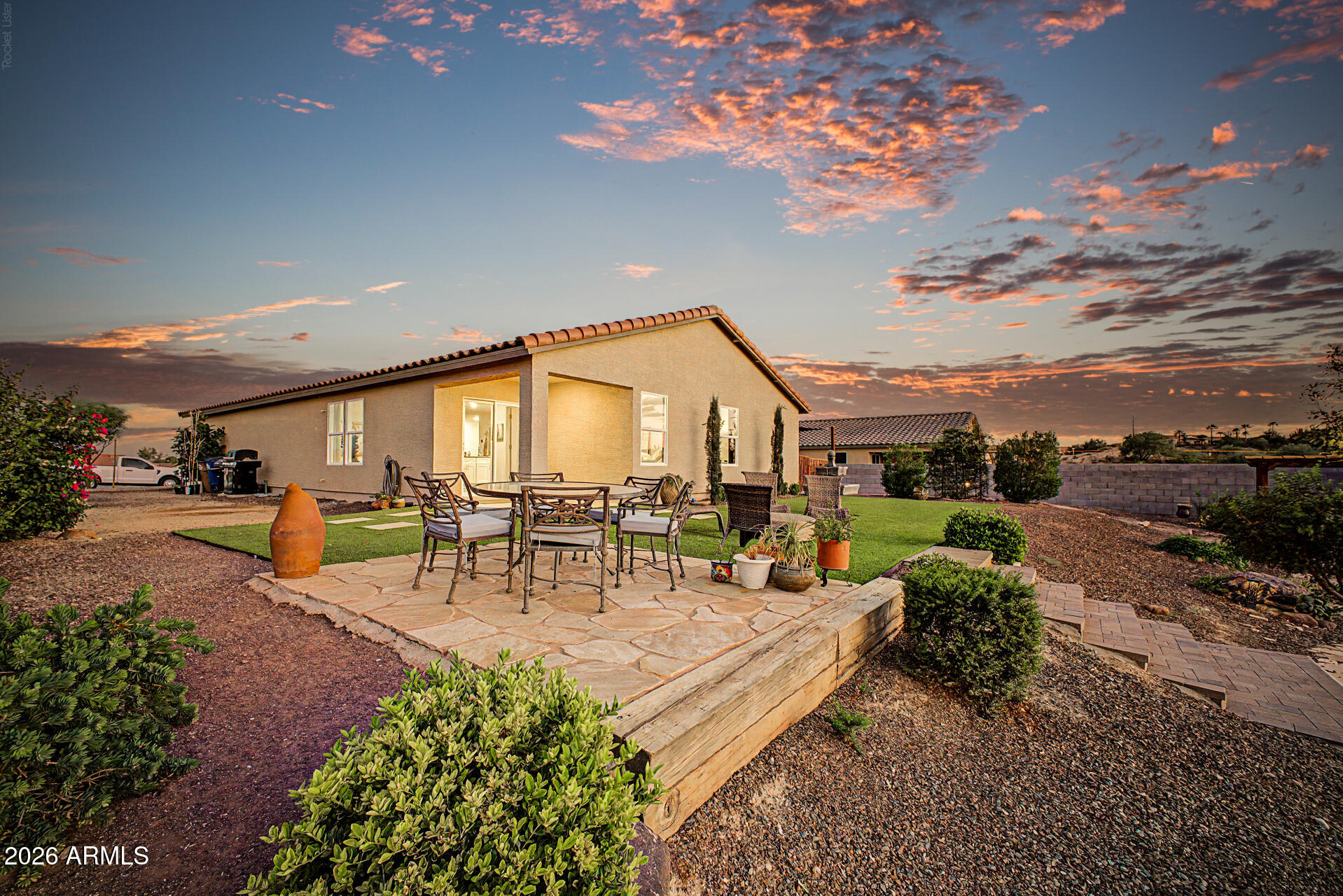 Home’s backyard patio with outdoor seating, raised lawn, and a vivid sunset sky.
