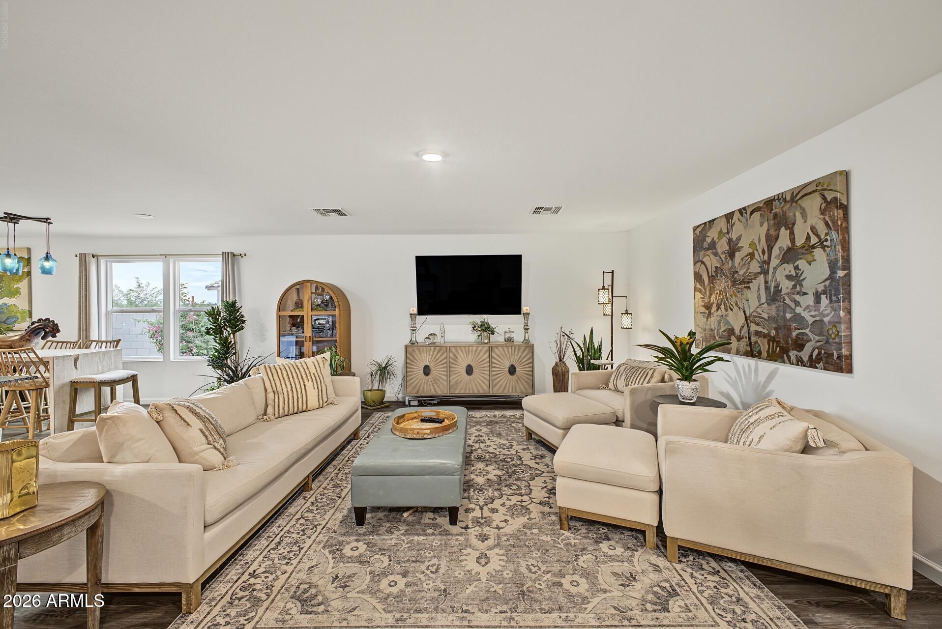 Furnished living room with cream sofas, patterned rug, wall-mounted television, and large botanical artwork.