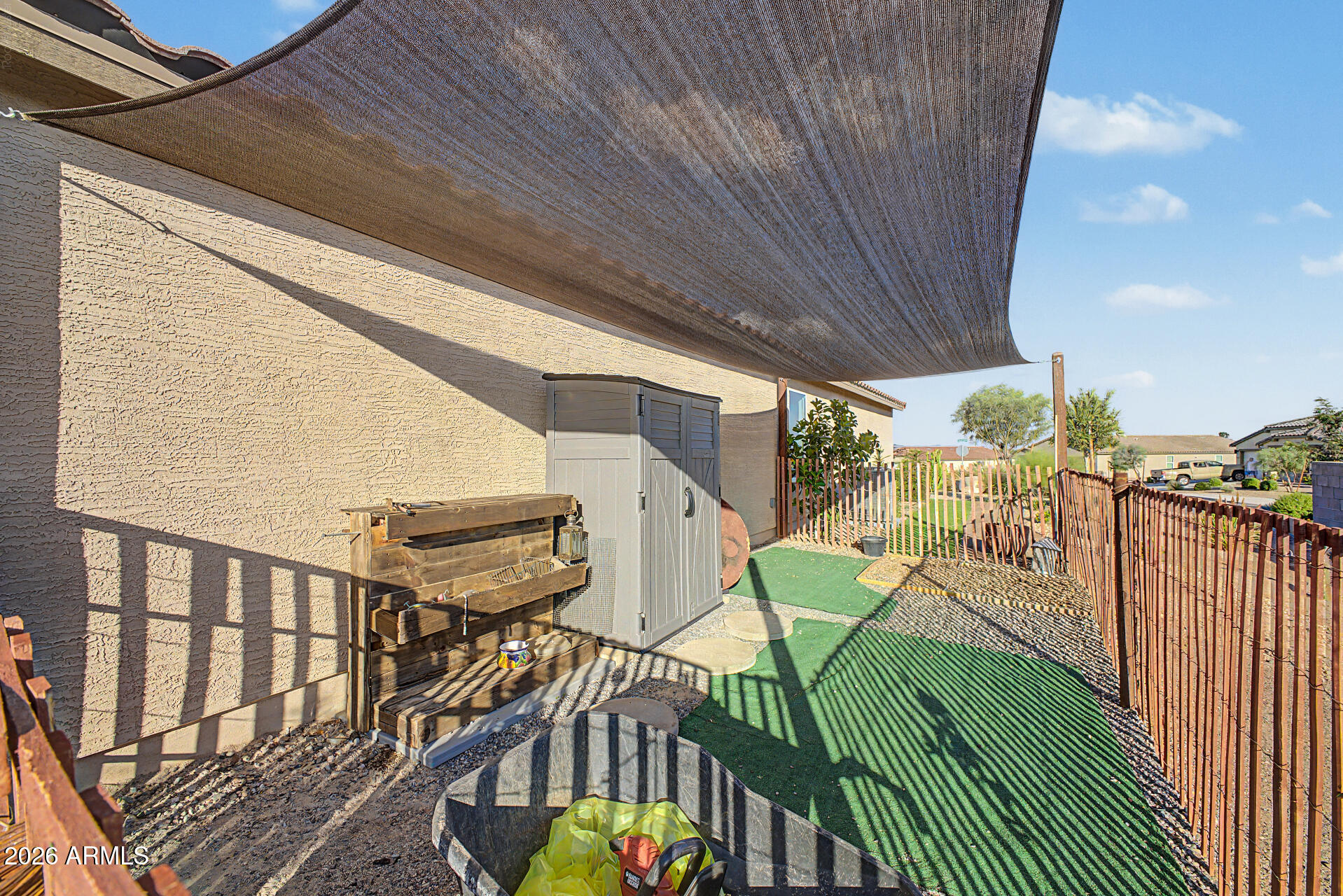 Backyard patio with a broad shade sail, artificial turf, and a fenced gravel border.