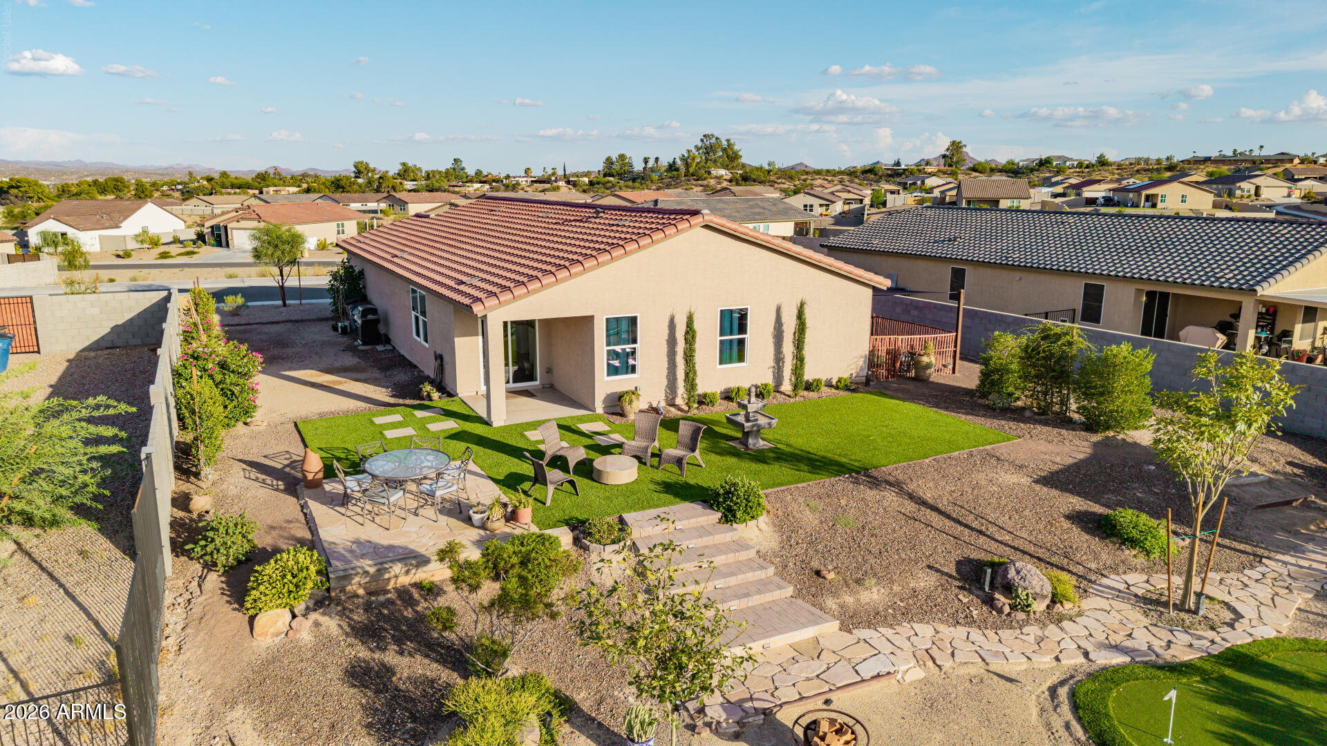 Aerial backyard view with artificial turf, patio seating, paver paths, and desert landscaping.