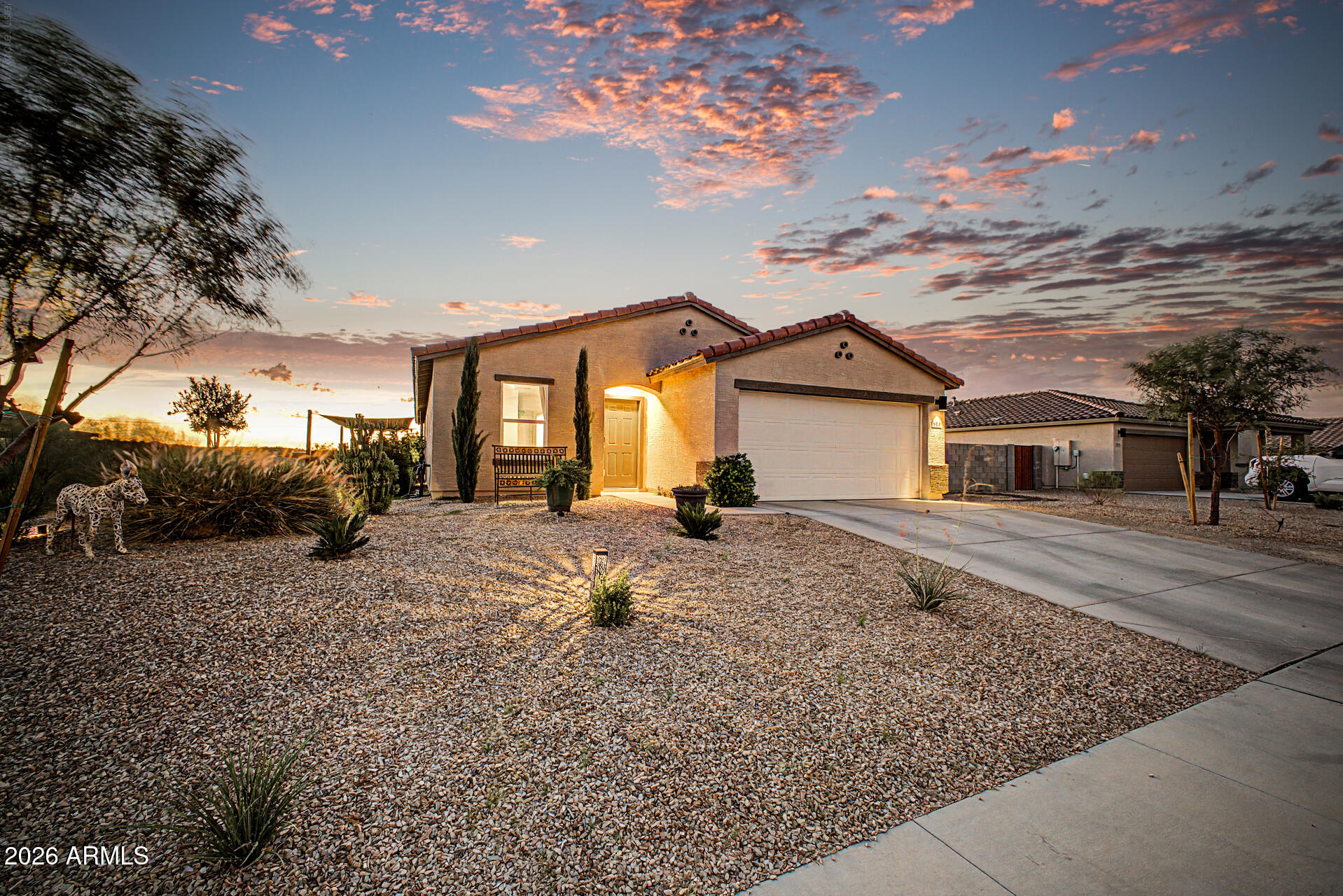 Stucco home with a tiled roof, two-car garage, and gravel desert landscaping at sunset.