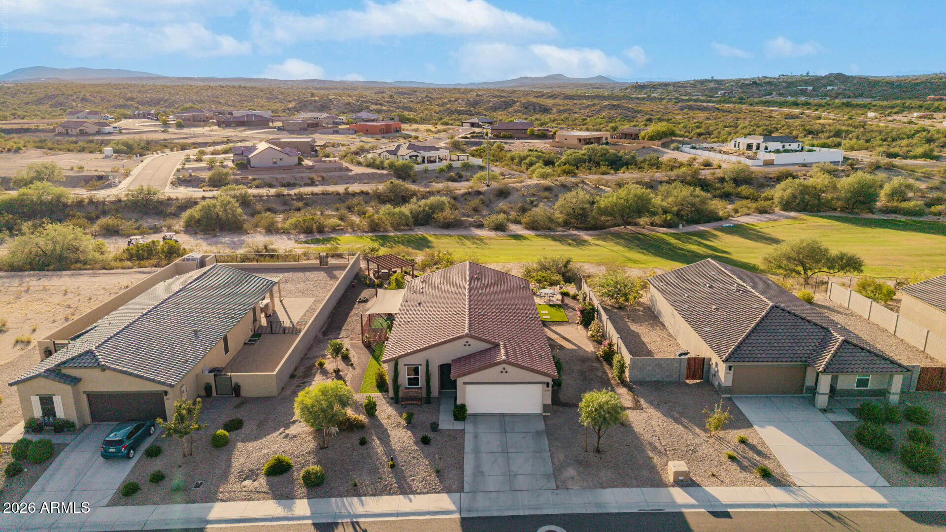 Aerial view of a tile-roof home with desert landscaping, neighboring houses, and distant hills.