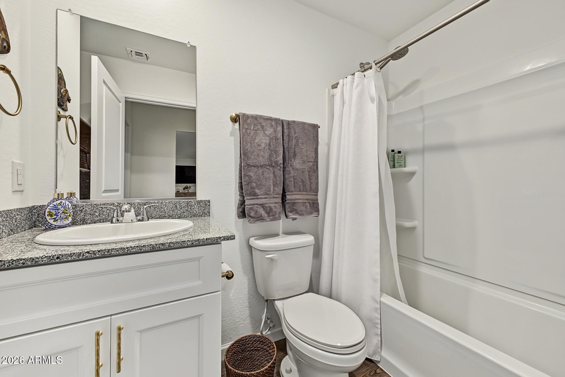 Bathroom with a granite-topped vanity, gray towels, and a white tub-shower.