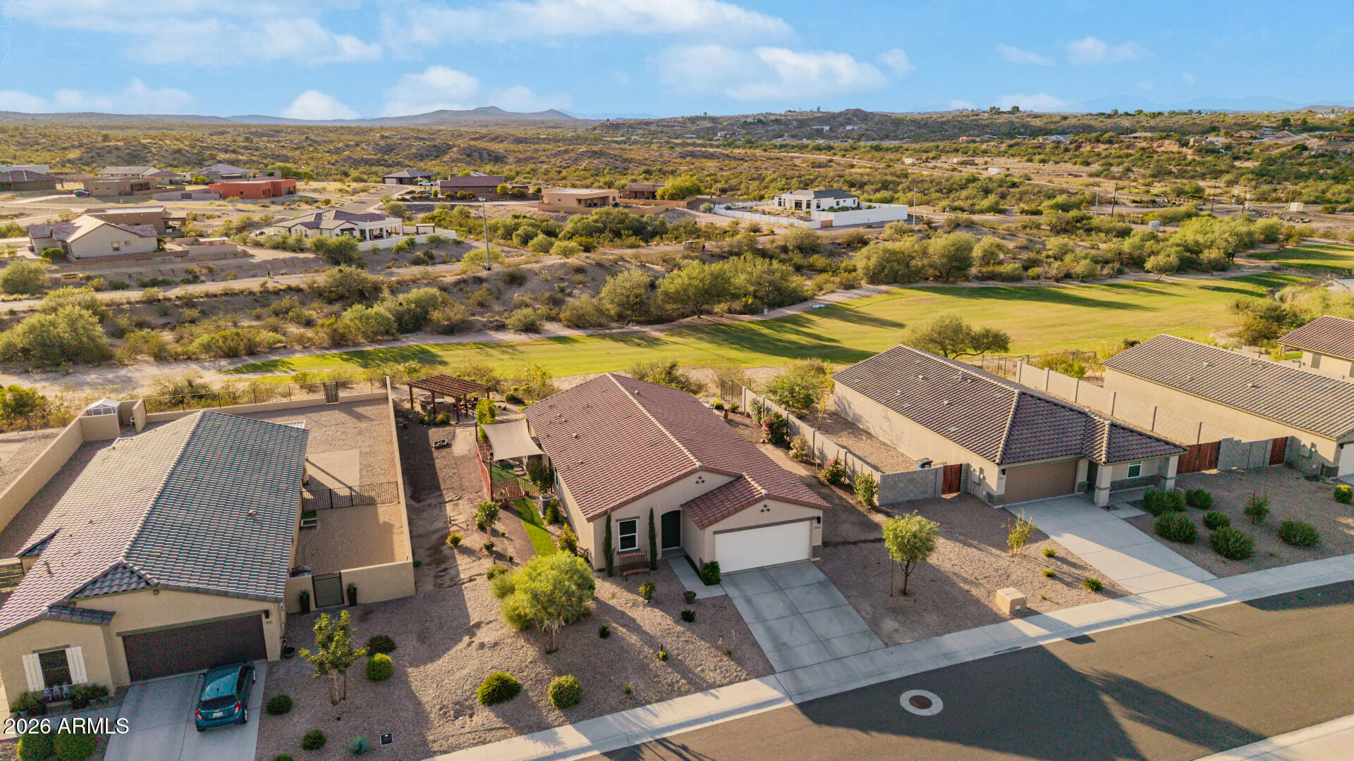 Aerial view of a desert home beside a manicured green lawn, with hills in the distance.