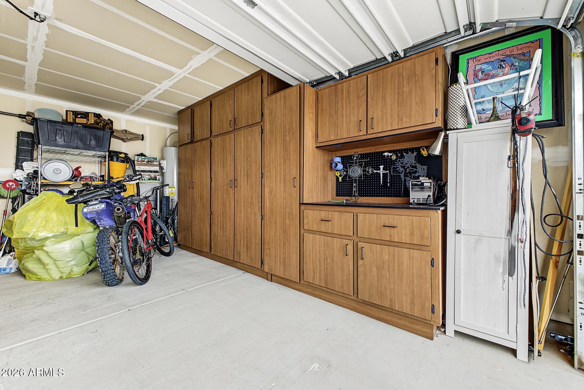 Garage with extensive wood cabinetry, a pegboard workbench, and bicycles and stored items.