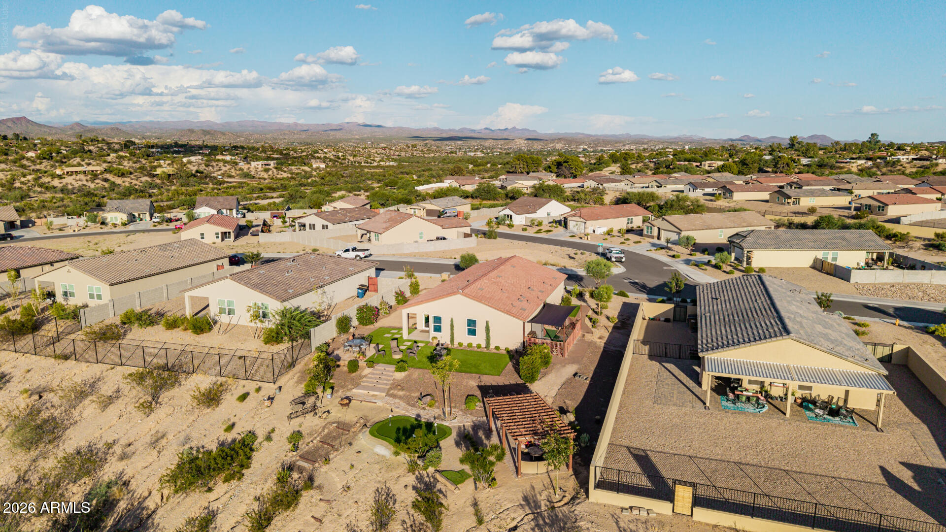 Aerial view of a desert home with a landscaped backyard, surrounded by homes and distant mountains.
