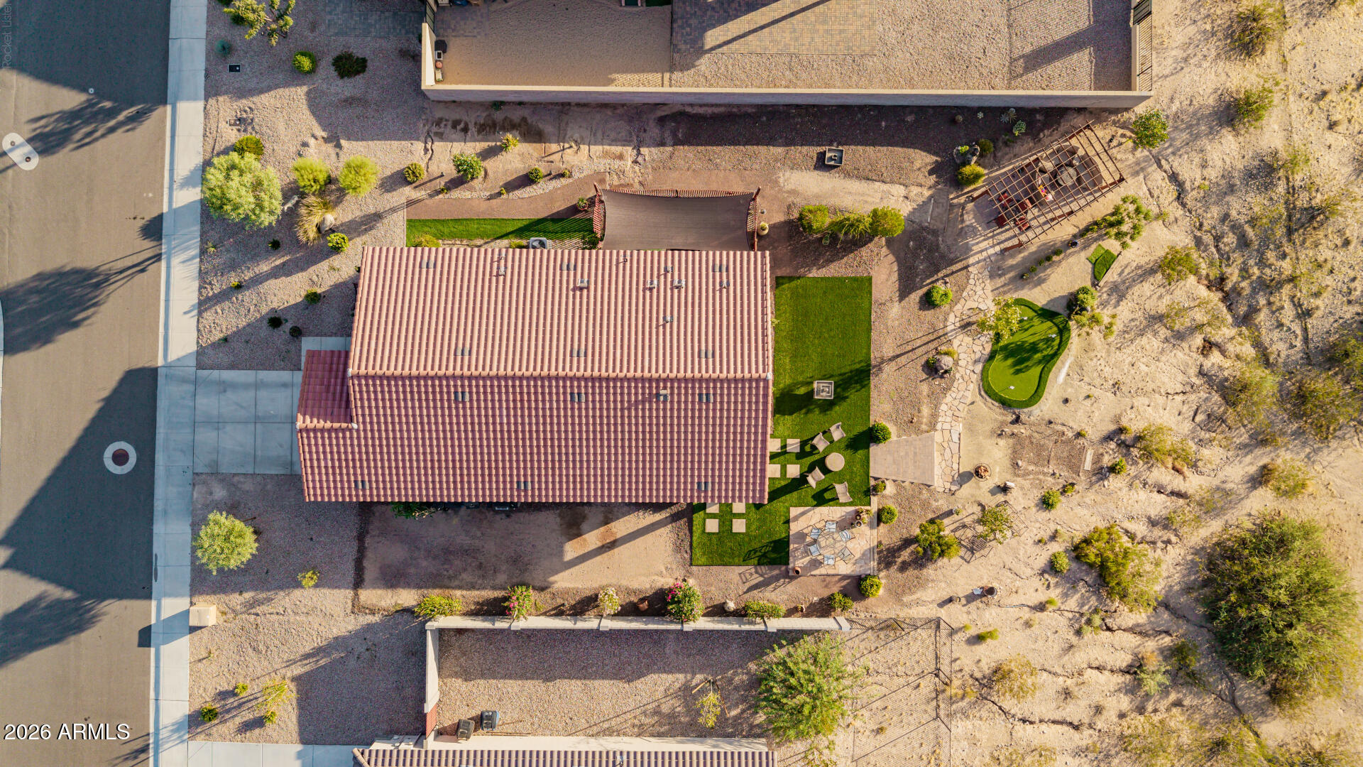 Aerial view of a home with a tiled roof, putting green, pergola, and desert landscaping.
