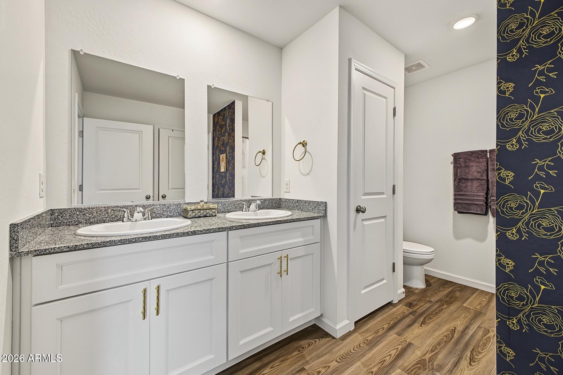 Bathroom with a white double vanity, speckled granite counter, and navy-and-gold floral wallpaper.