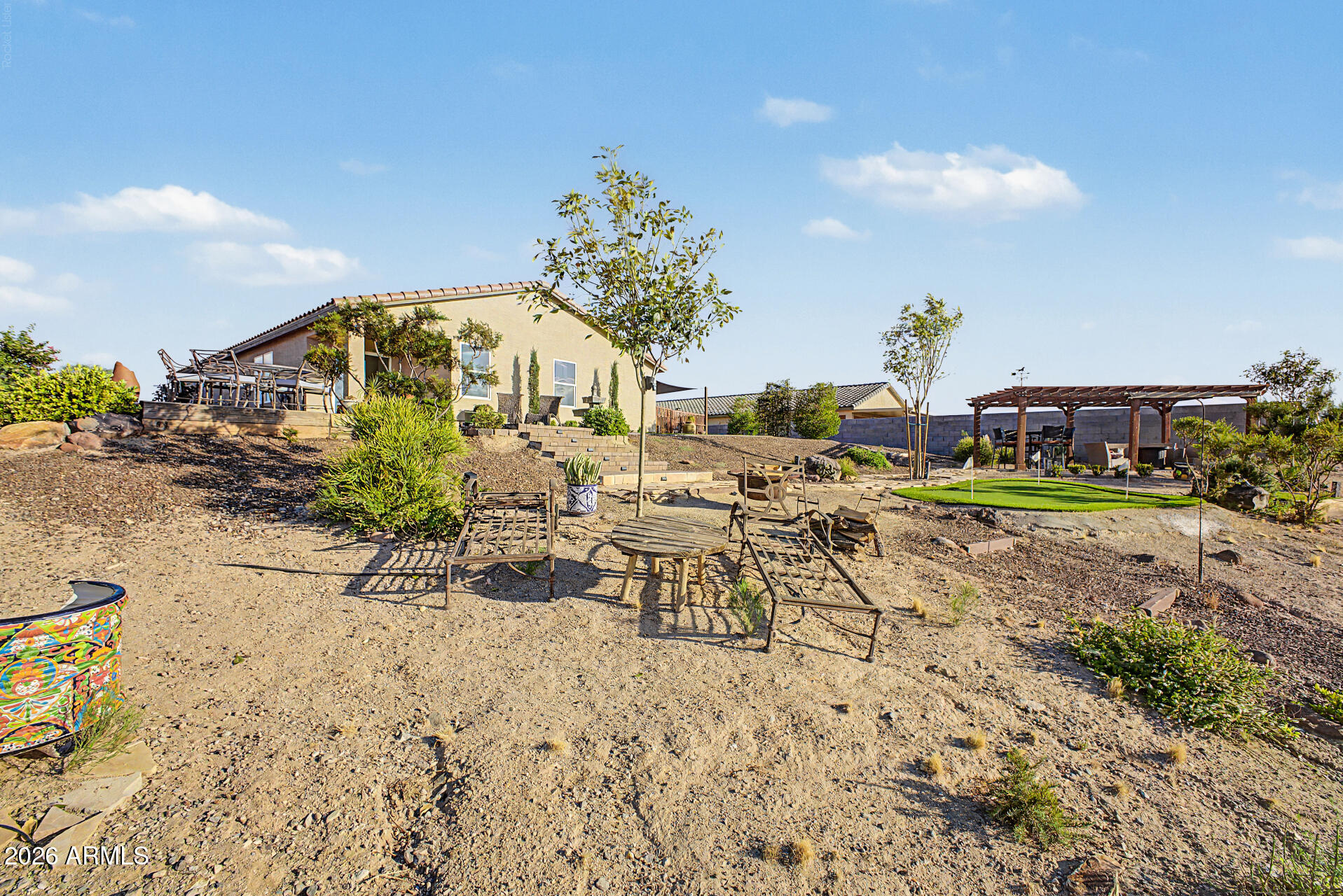 Backyard with gravel landscaping, outdoor seating, and a pergola beside a tan stucco home.