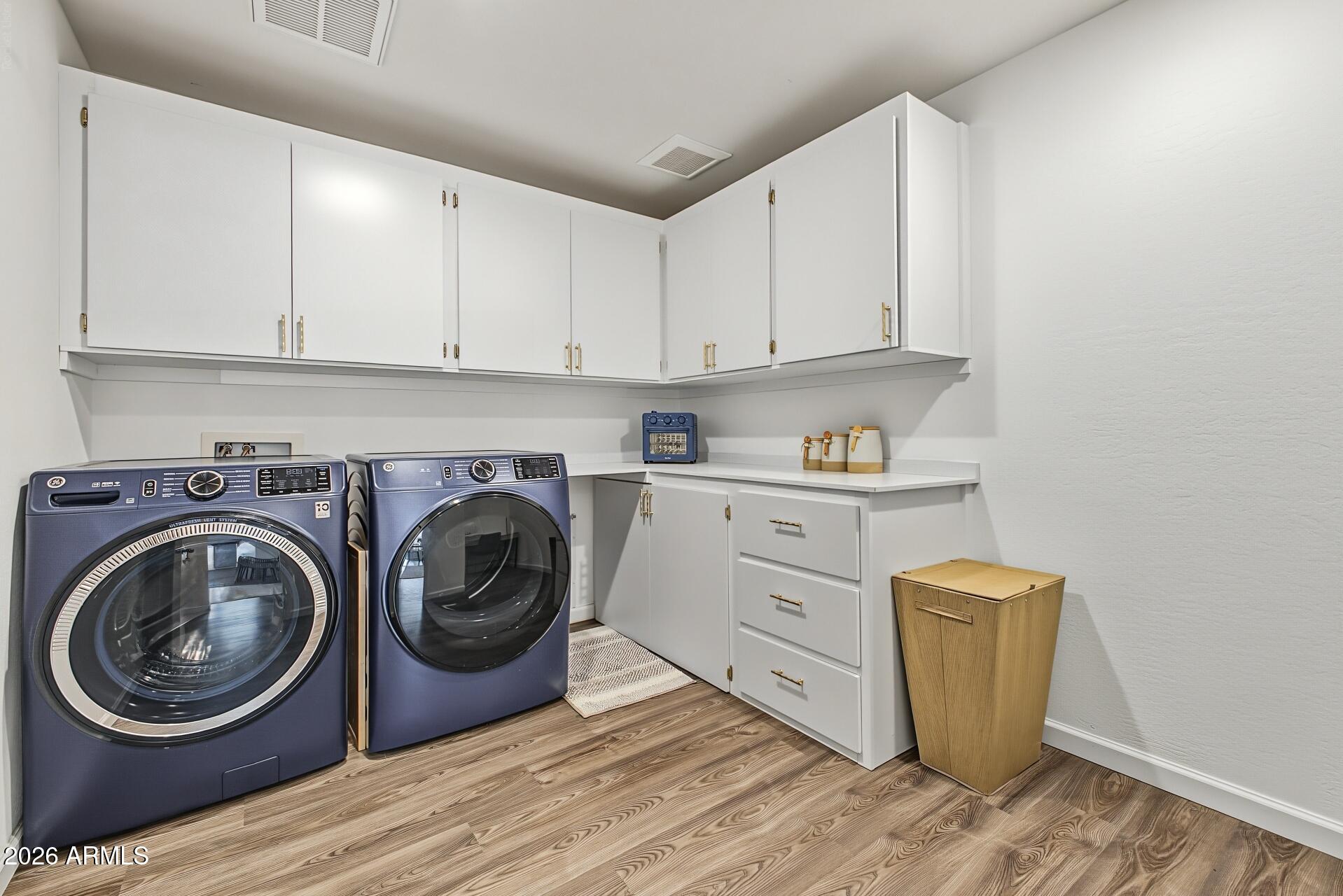 Laundry room with blue front-loading washer and dryer, white cabinetry, and wood-look floors.