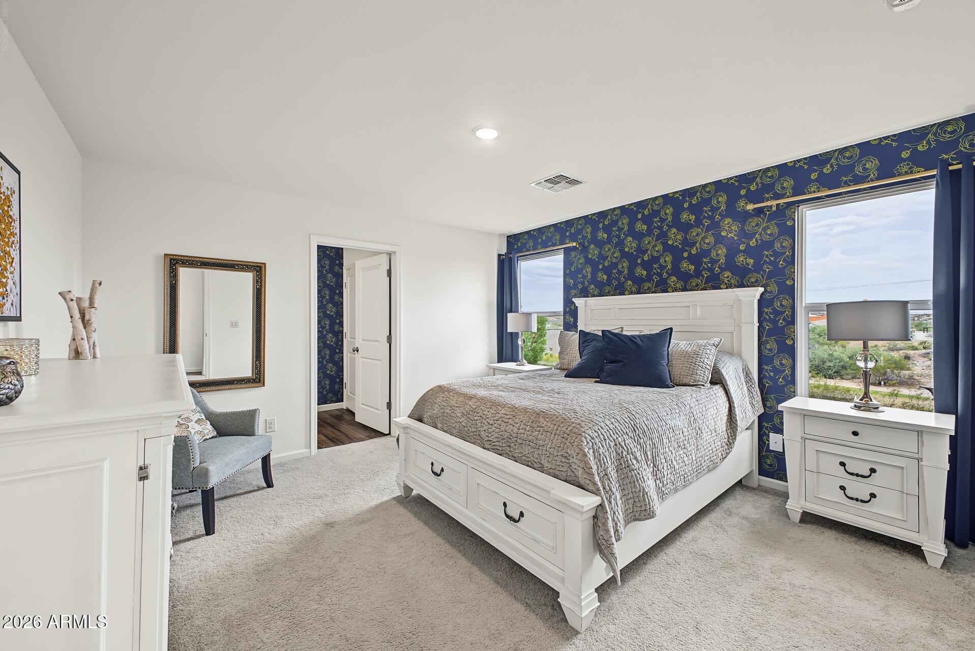 Bedroom with a white bed, navy floral wallpaper, and two large windows.