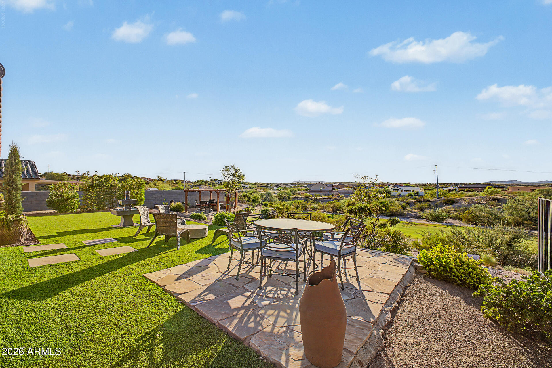 Backyard patio with outdoor dining set, green lawn, fountain, and distant desert hills.