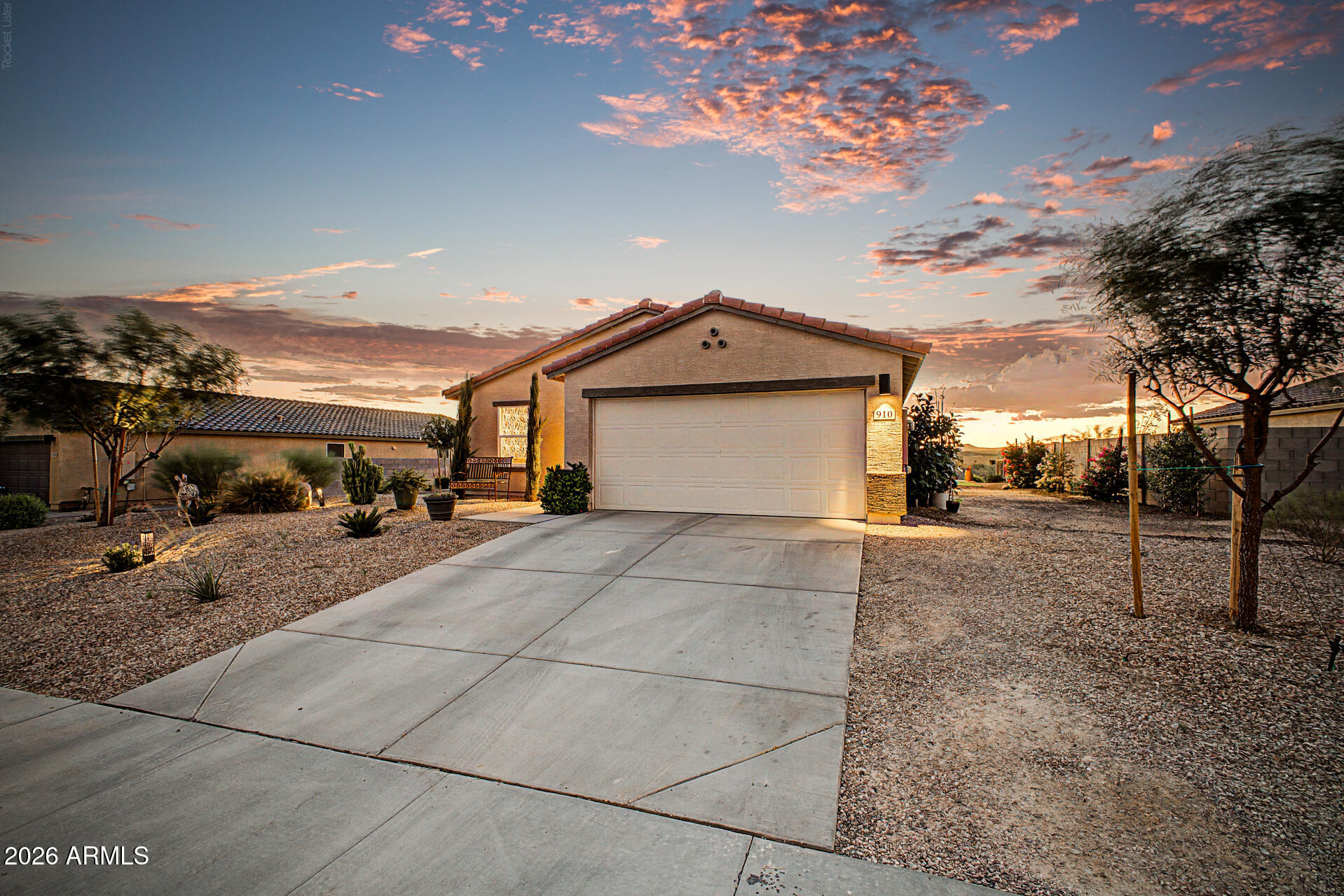 Single-story stucco home with a two-car garage, desert landscaping, and a colorful dusk sky.