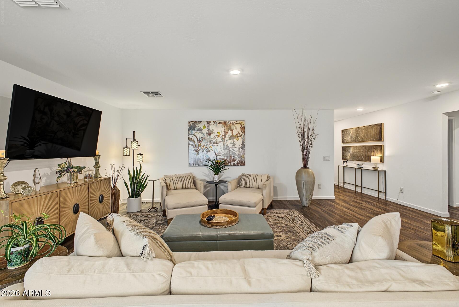 Furnished living room with a white sectional, cream armchairs, hardwood floors, and contemporary artwork.