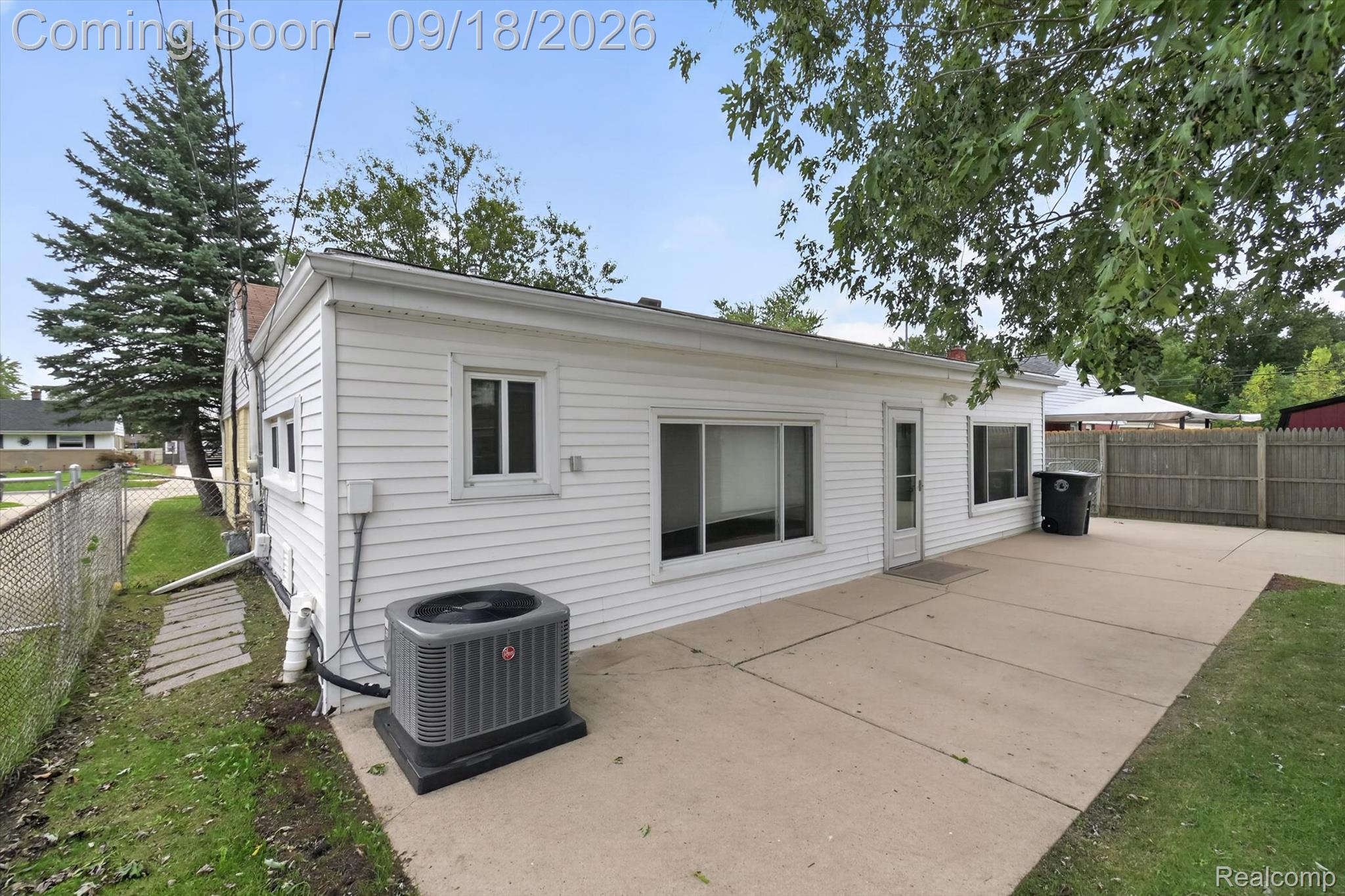 White-sided house with a broad concrete patio and an outdoor air-conditioning unit.