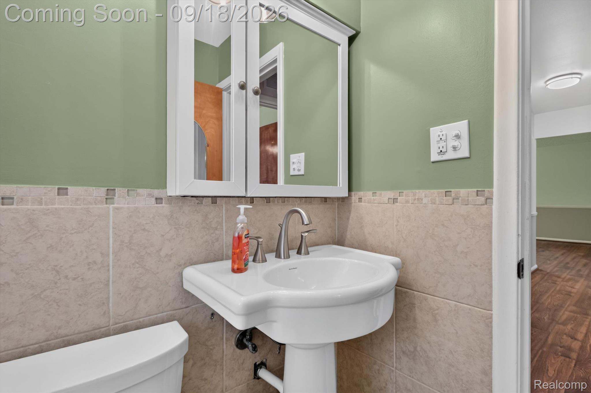 Bathroom with a white pedestal sink, mirrored cabinet, and beige tile walls.