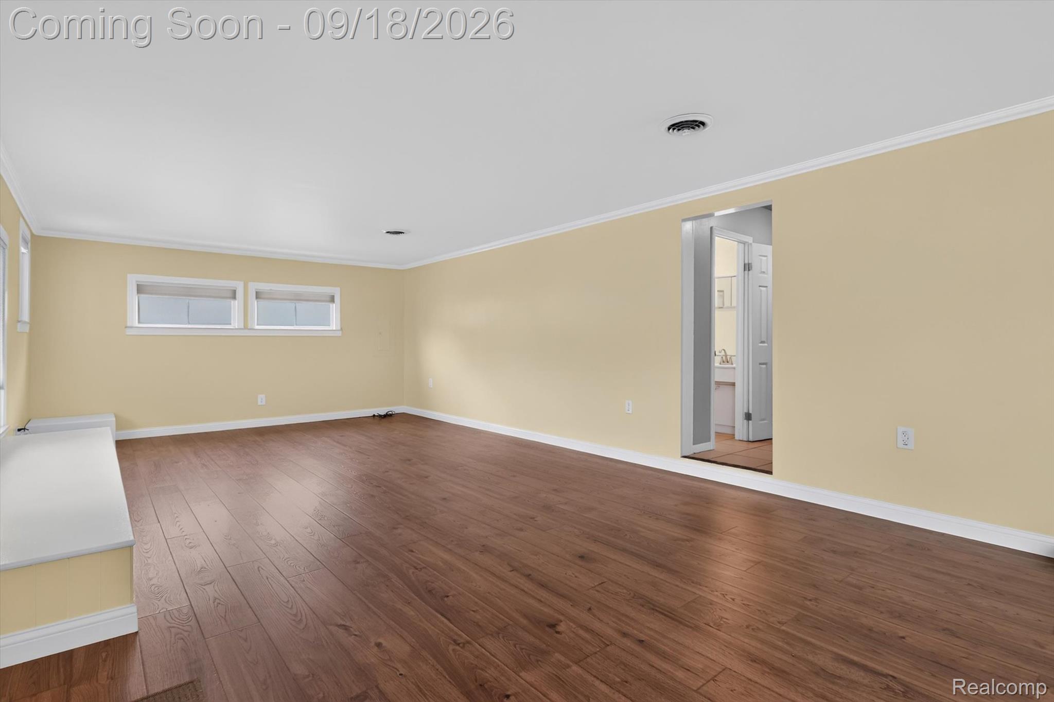 Empty room with pale yellow walls, wide-plank brown flooring, and an open doorway to a bathroom.