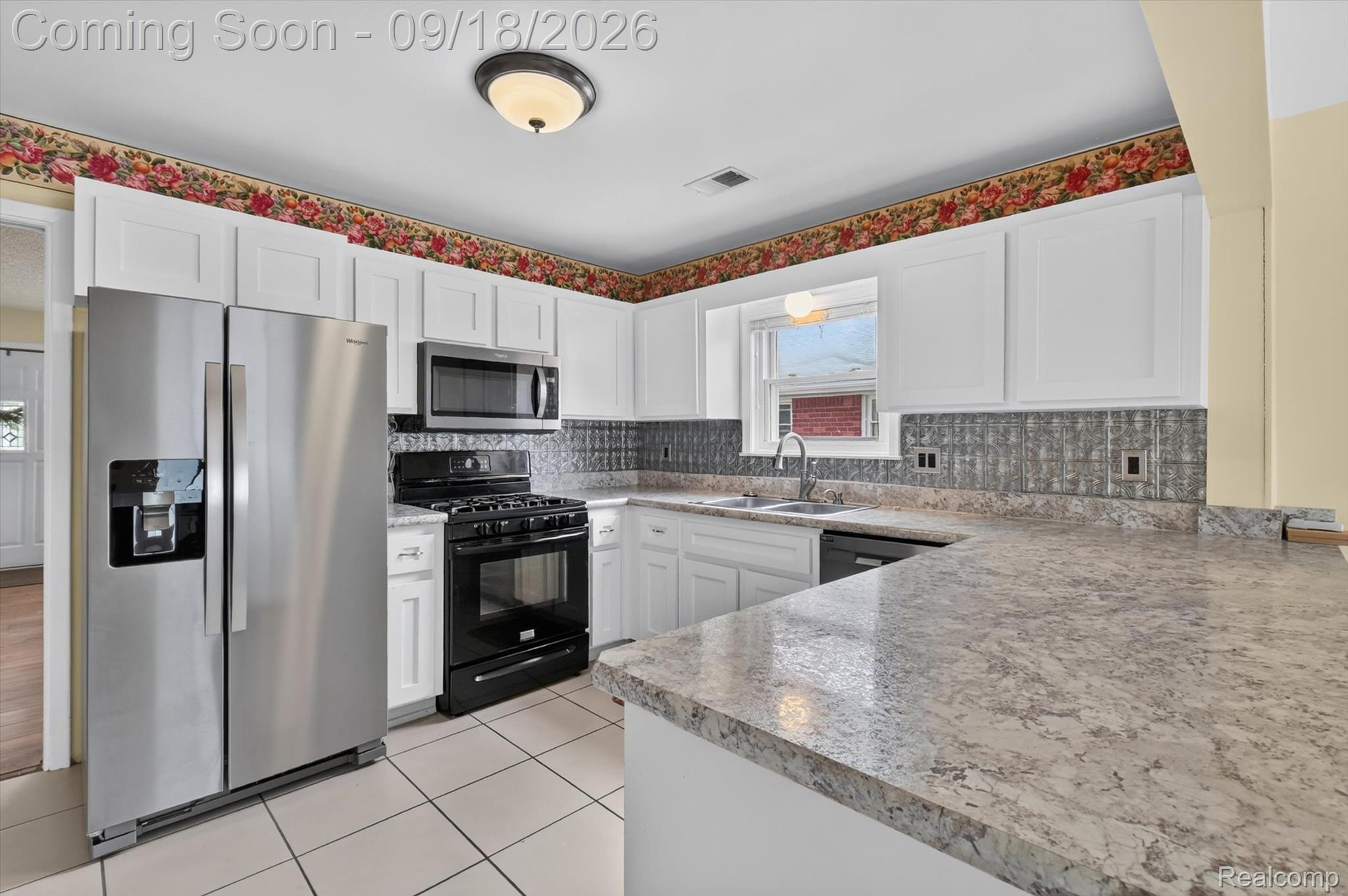 Kitchen with white cabinets, granite peninsula, stainless refrigerator, patterned backsplash, and floral border.