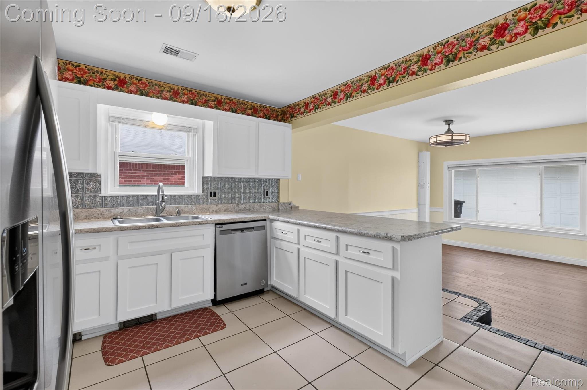 Kitchen with white cabinets, a stone peninsula, stainless steel appliances, and a floral wallpaper border.