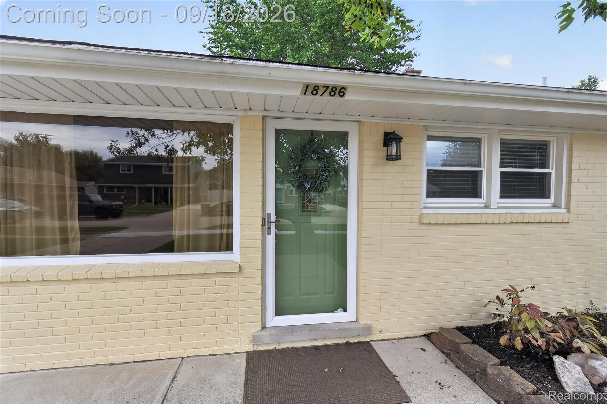 Home entrance with pale yellow brick, green glass storm door, and house number 18786.