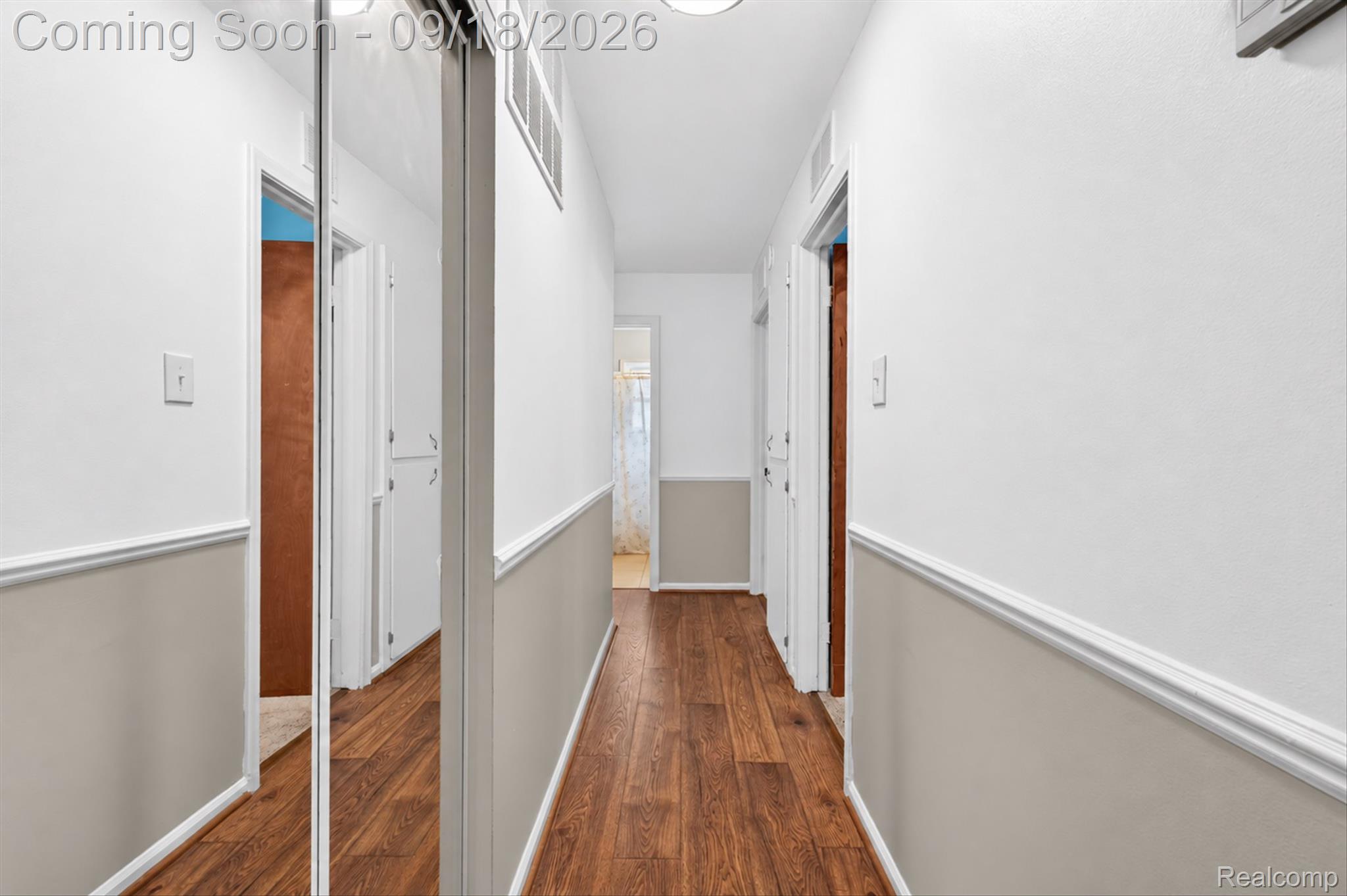 Hallway with warm wood-look flooring, two-tone walls, and a mirrored closet door.
