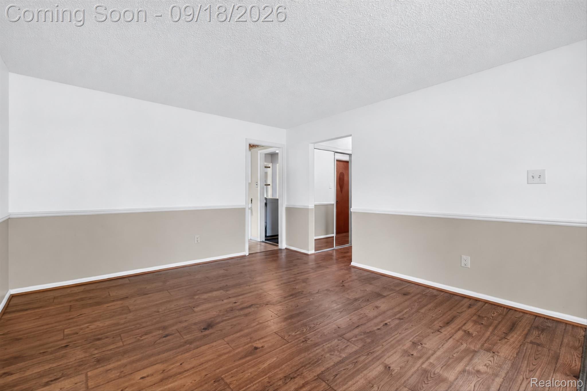 Empty living room with wood plank floors, taupe-and-white walls, and mirrored closet doors.