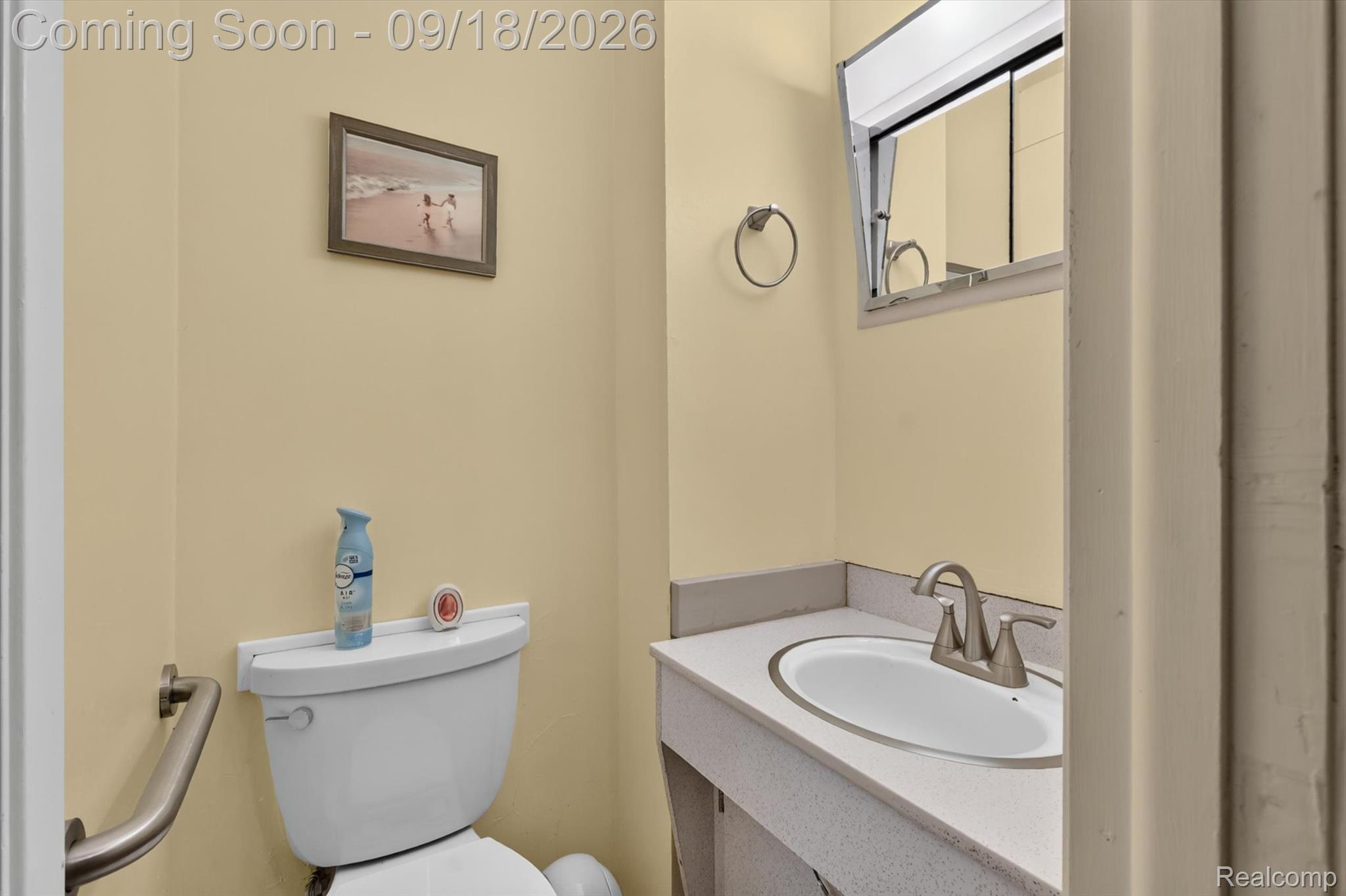 Bathroom with yellow walls, white toilet, grab bar, and speckled vanity with oval sink.