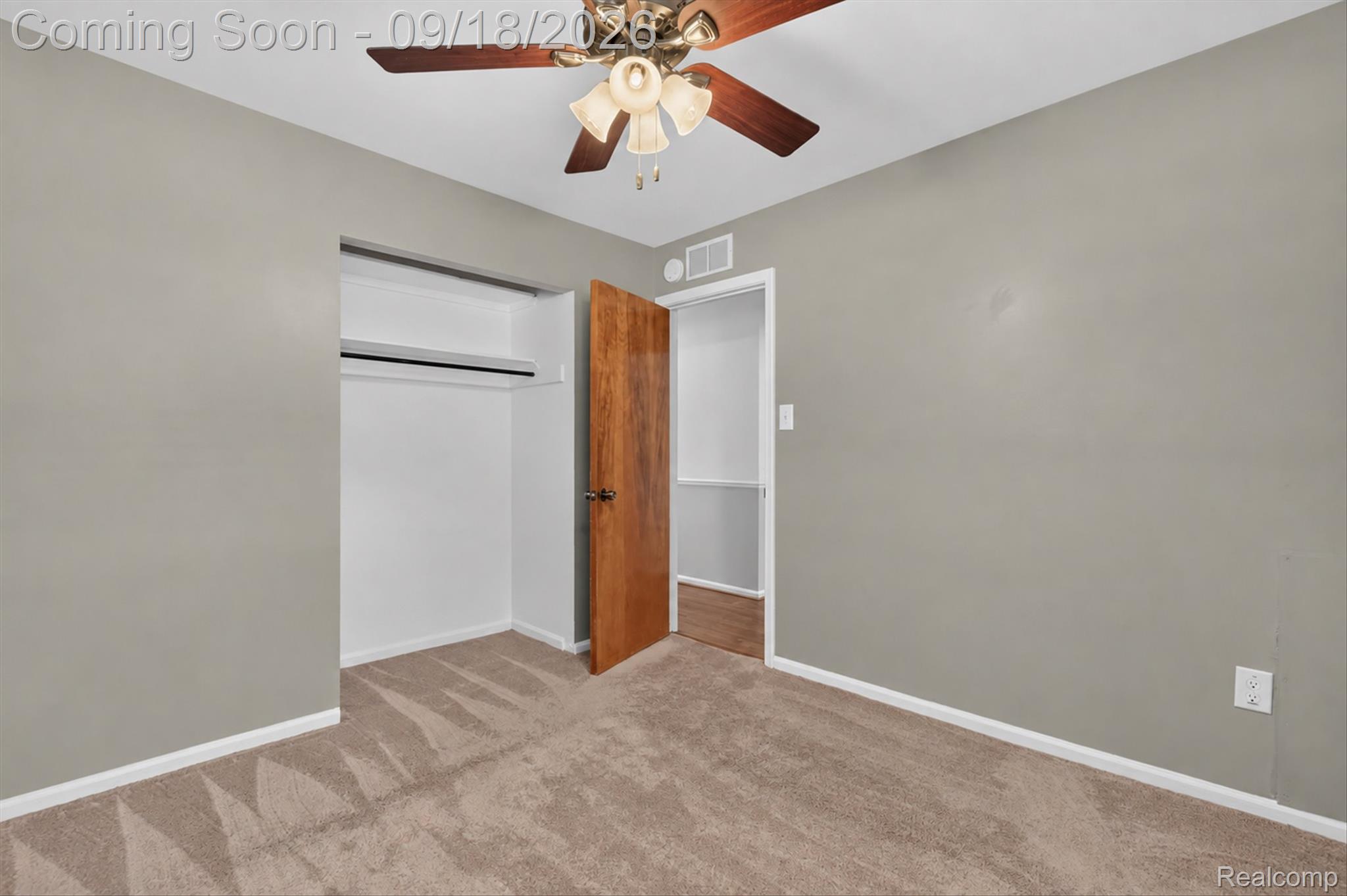 Empty carpeted bedroom with an open closet, wooden door, and ceiling fan.