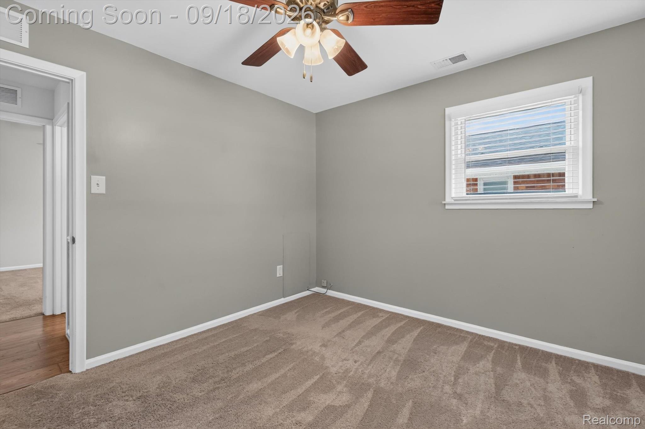 Empty bedroom with beige carpet, a ceiling fan, and a window with white blinds.